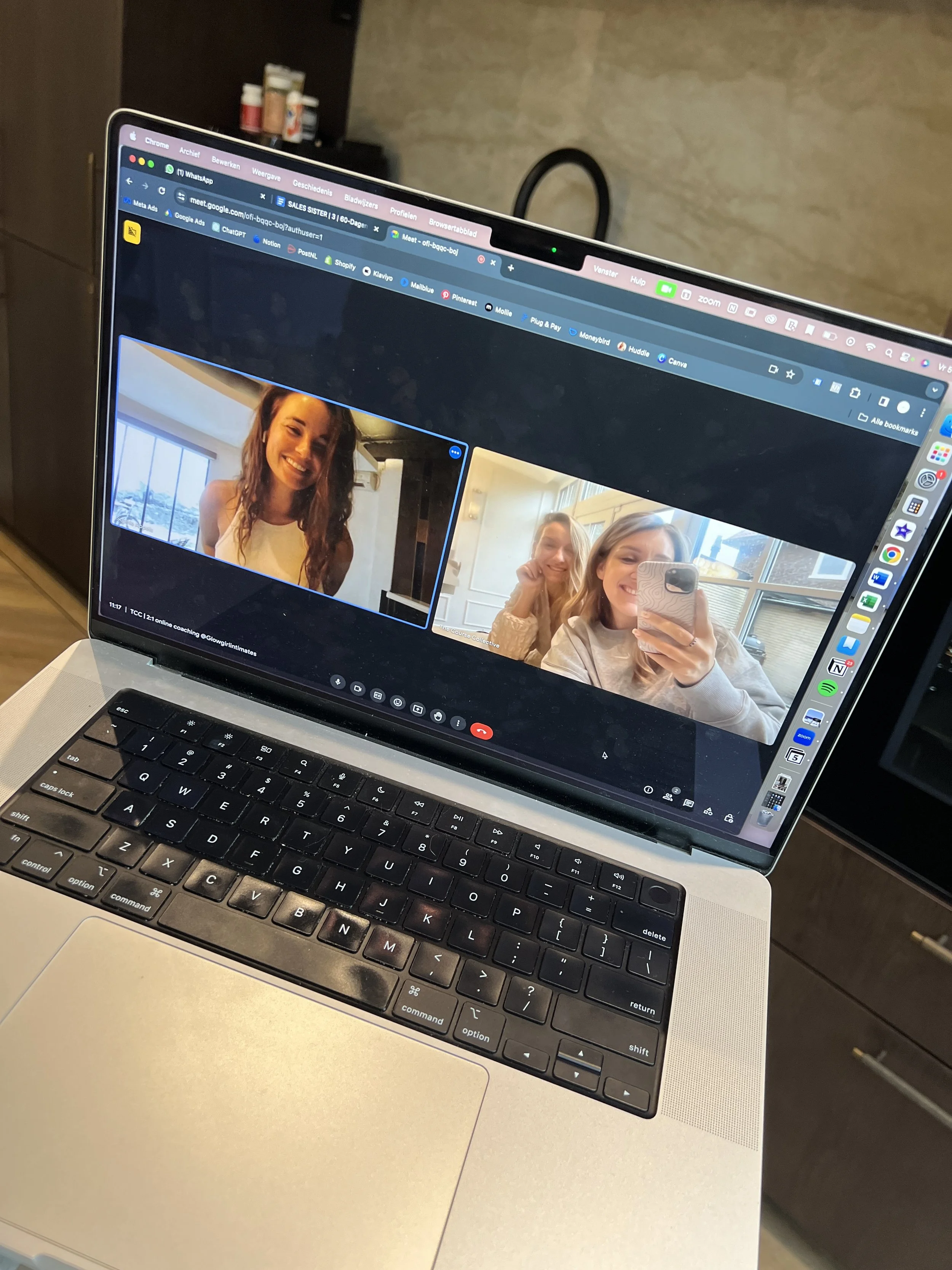 Laptop met open Zoom-vergadering waarbij drie vrouwen genieten en lachen, met een vrouw die foto's maakt met haar telefoon.