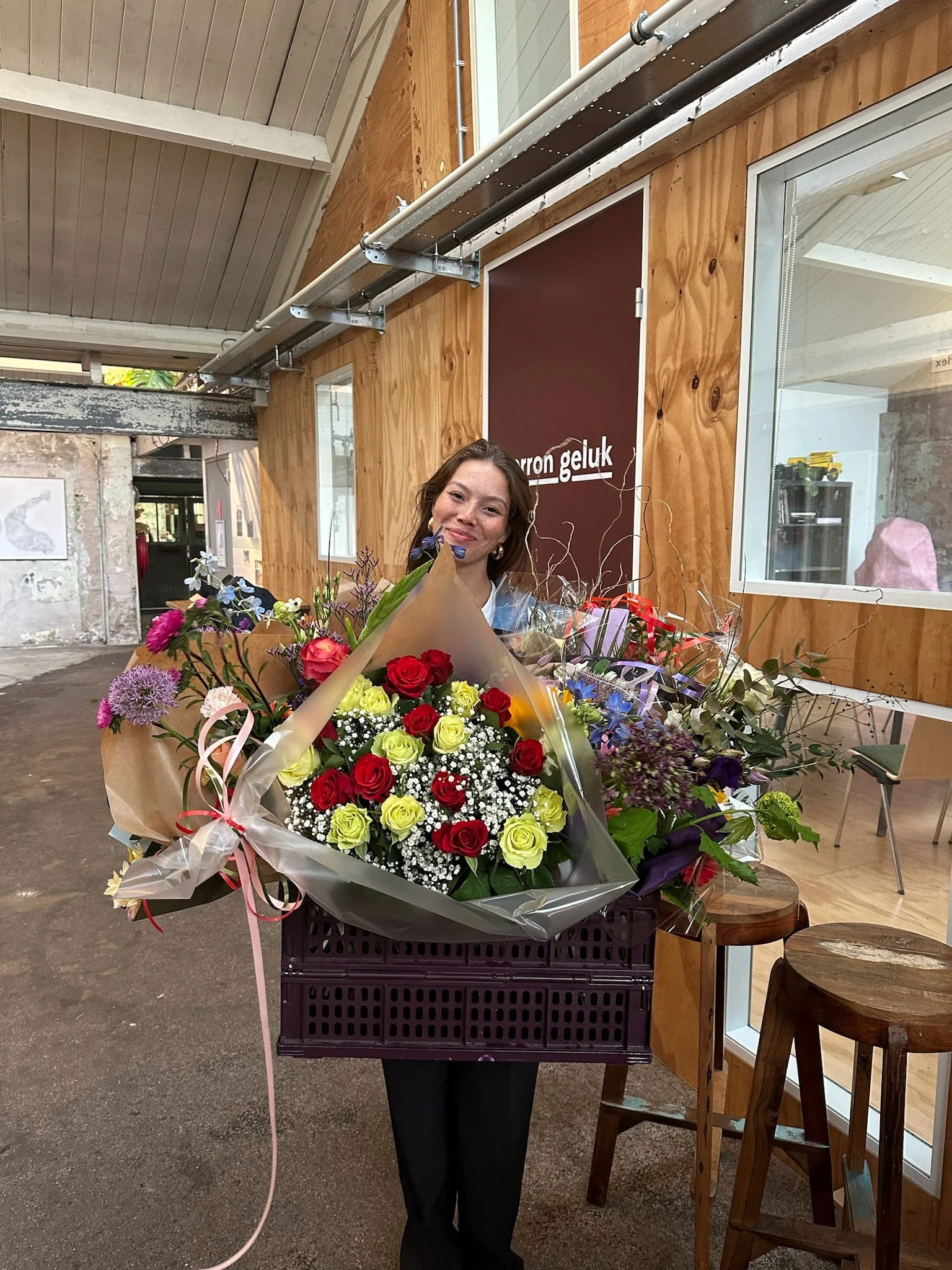 Vrouw met lange haar die bloemen vasthoudt in een interieur met houten muren en grote ramen.
