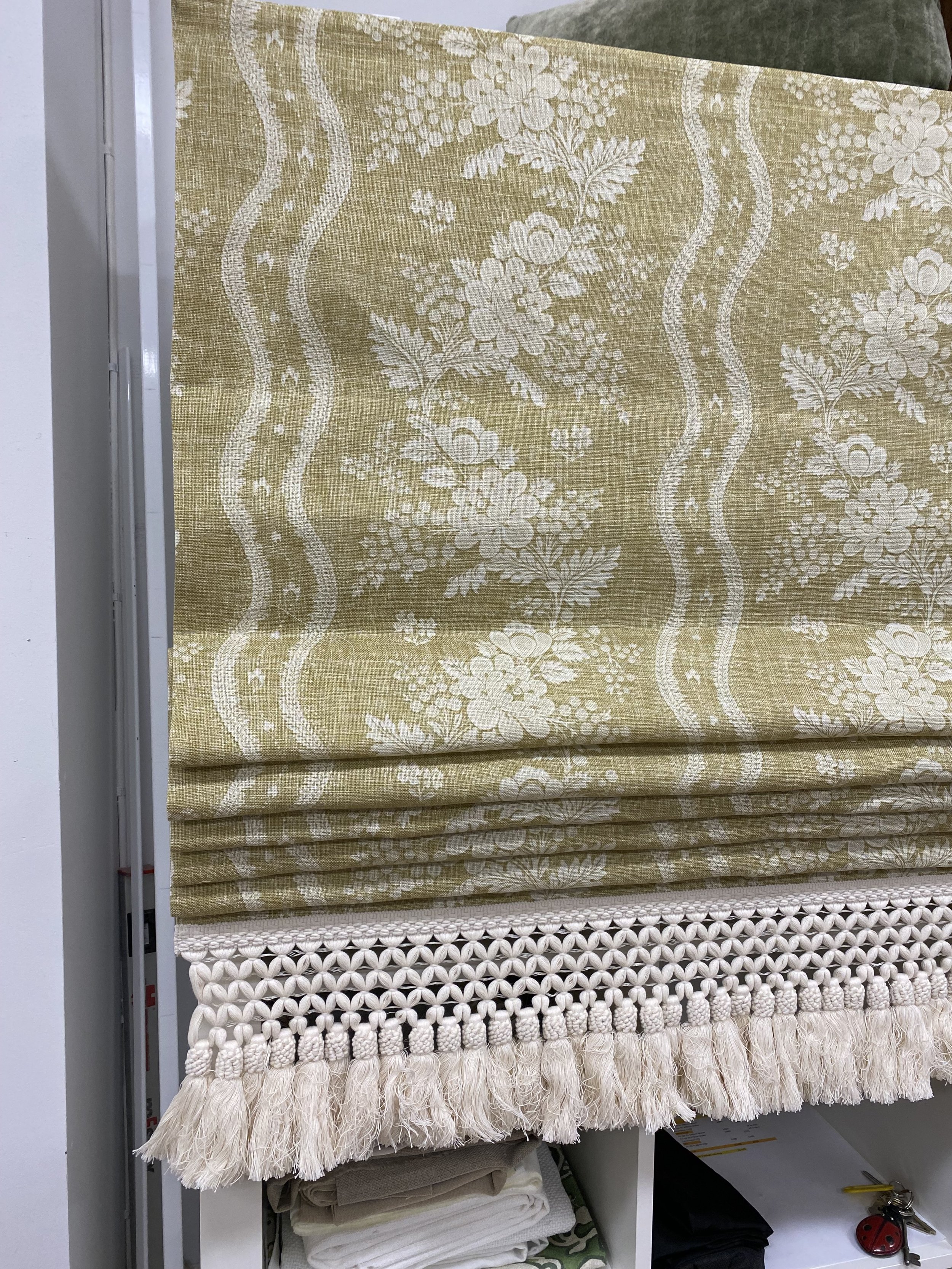 A display of fabric samples with floral patterns and different weave textures, including a decorative edge with tassels and pom-poms.