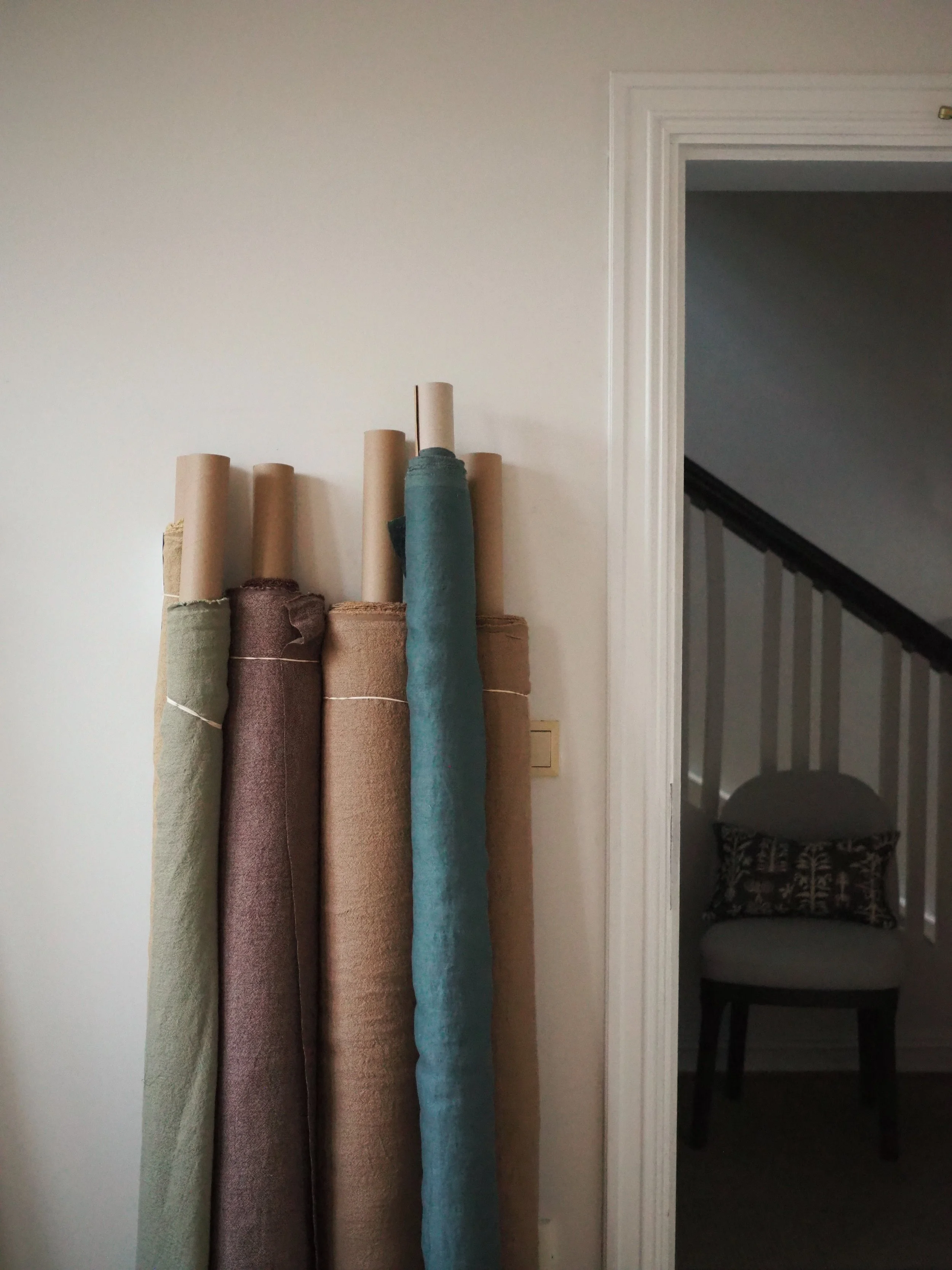 A collection of rolled-up carpets in various colors leaning against a white wall next to a doorway.