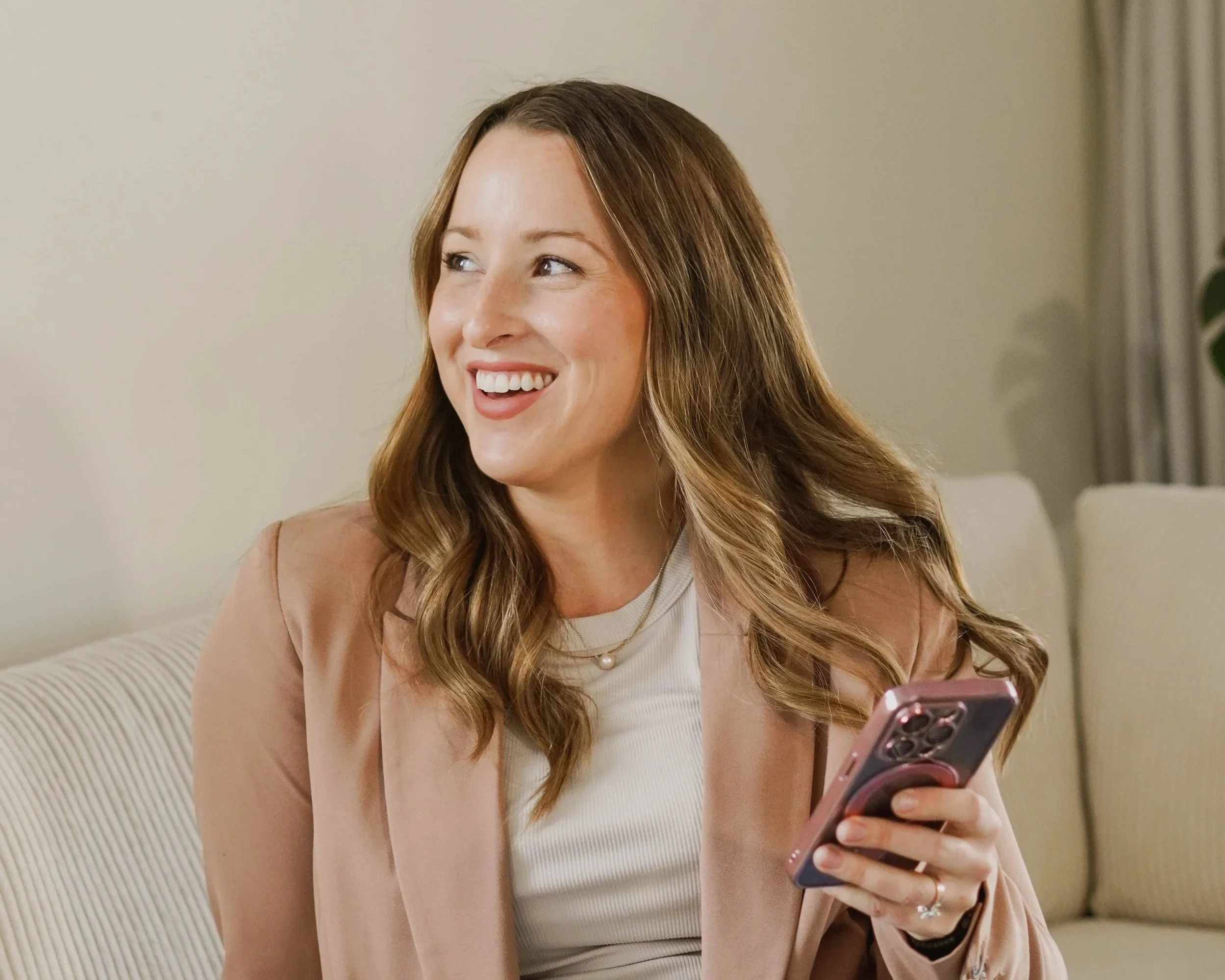 A woman sitting on a couch smiling and holding a smartphone.