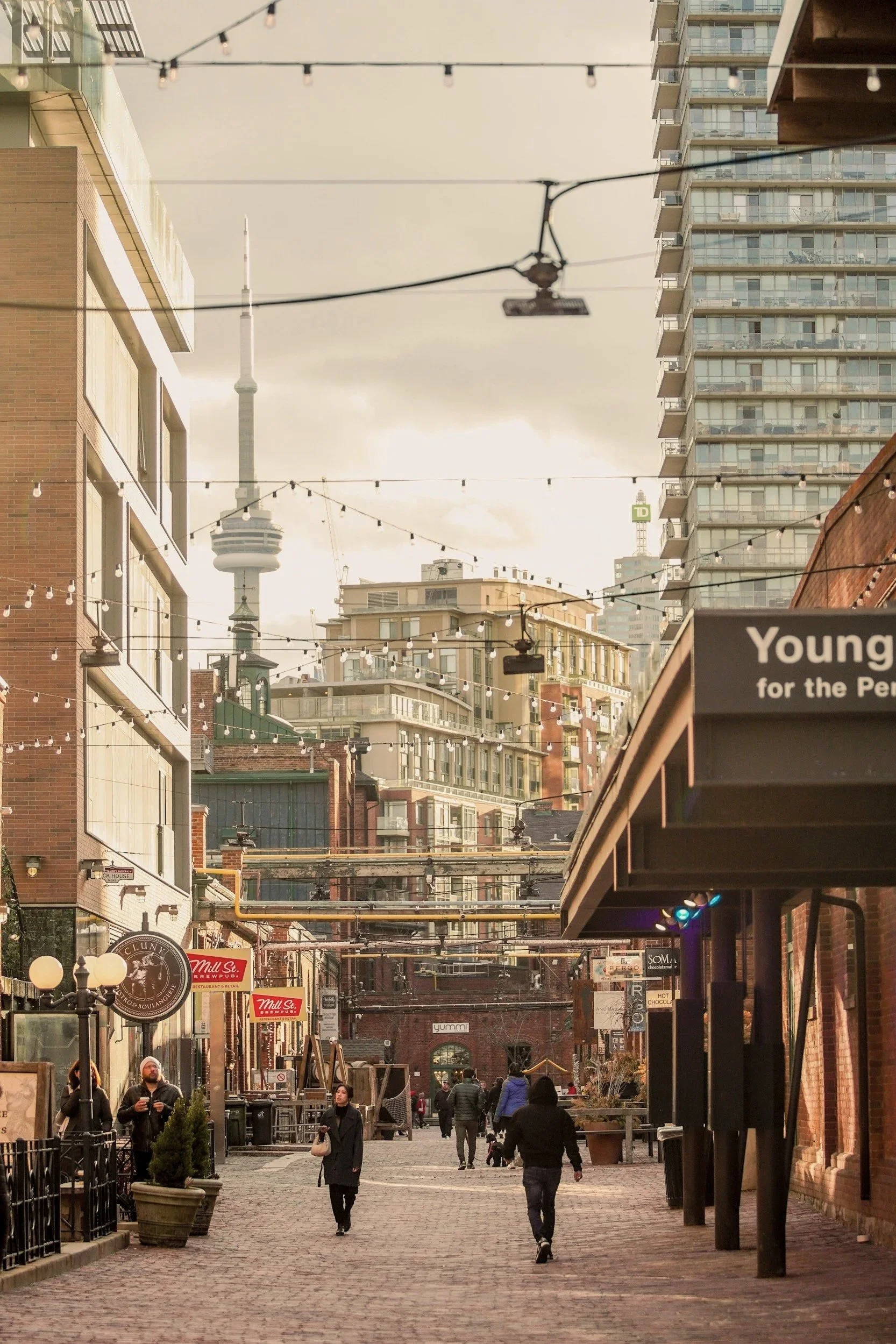 The Distillery District in Toronto. There are people walking along the Distillery shops. The CN Tower can be seen in the distance.