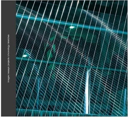 Close-up of a metal fence with diagonal white lines overlayed, part of a large modern building with glass windows in the background.