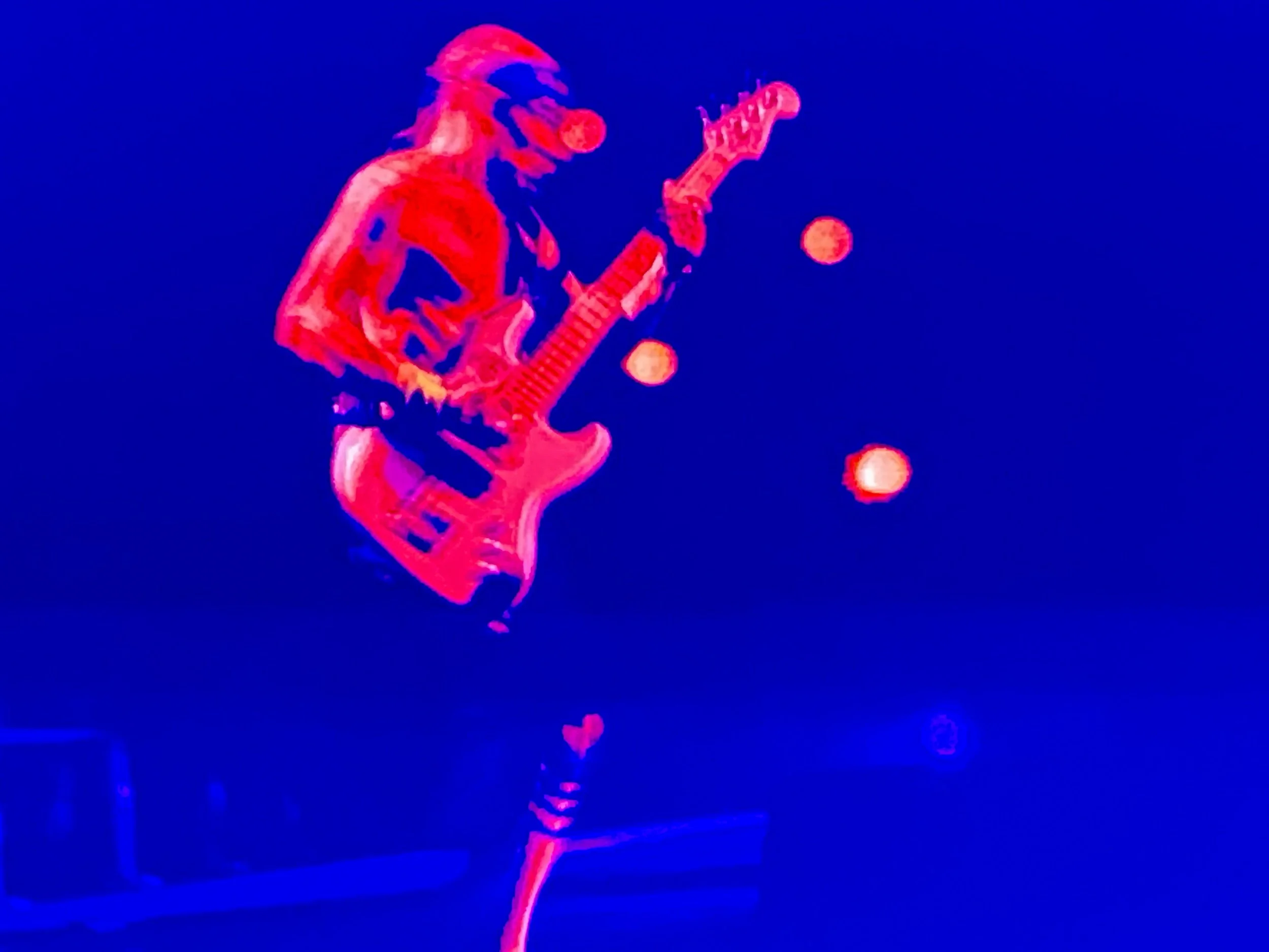 A neon-lit illustration of a guitarist playing an electric guitar on stage, with three orange spotlights in the background.