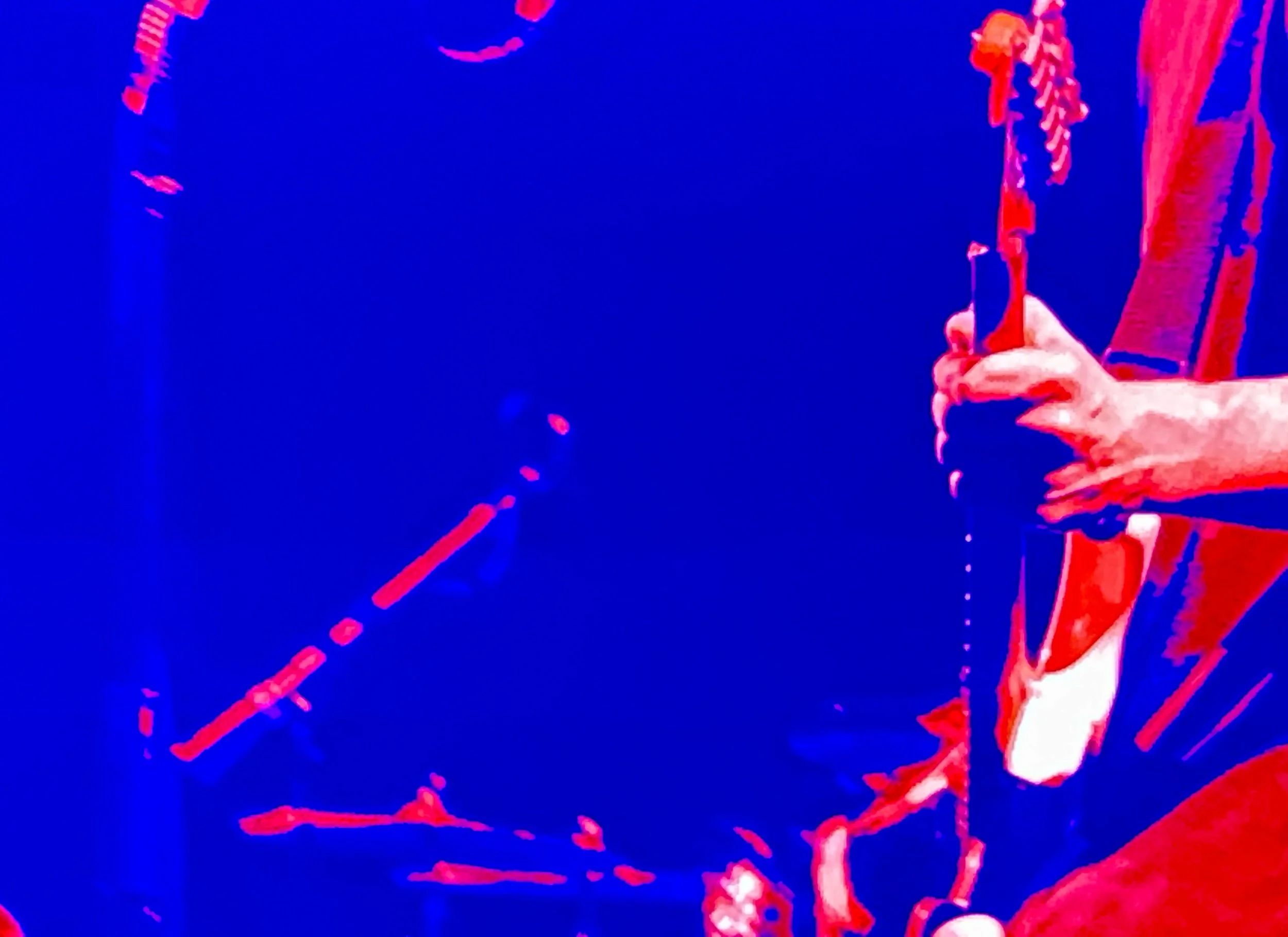 Person playing a guitar on stage, with vivid red and blue lighting.