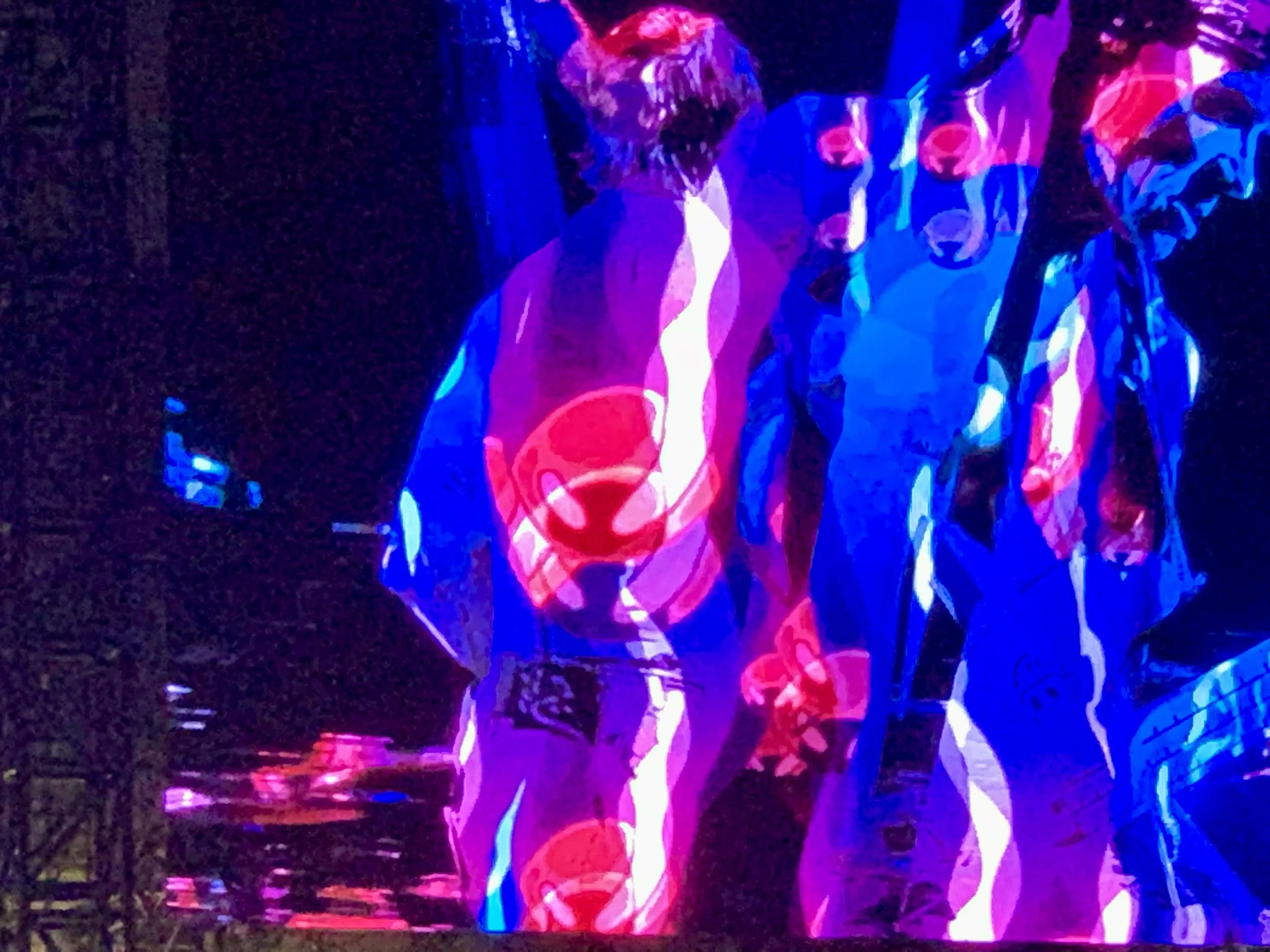 Two individuals are illuminated by colorful, abstract neon light patterns on a dark background, creating a vibrant, artistic visual effect.