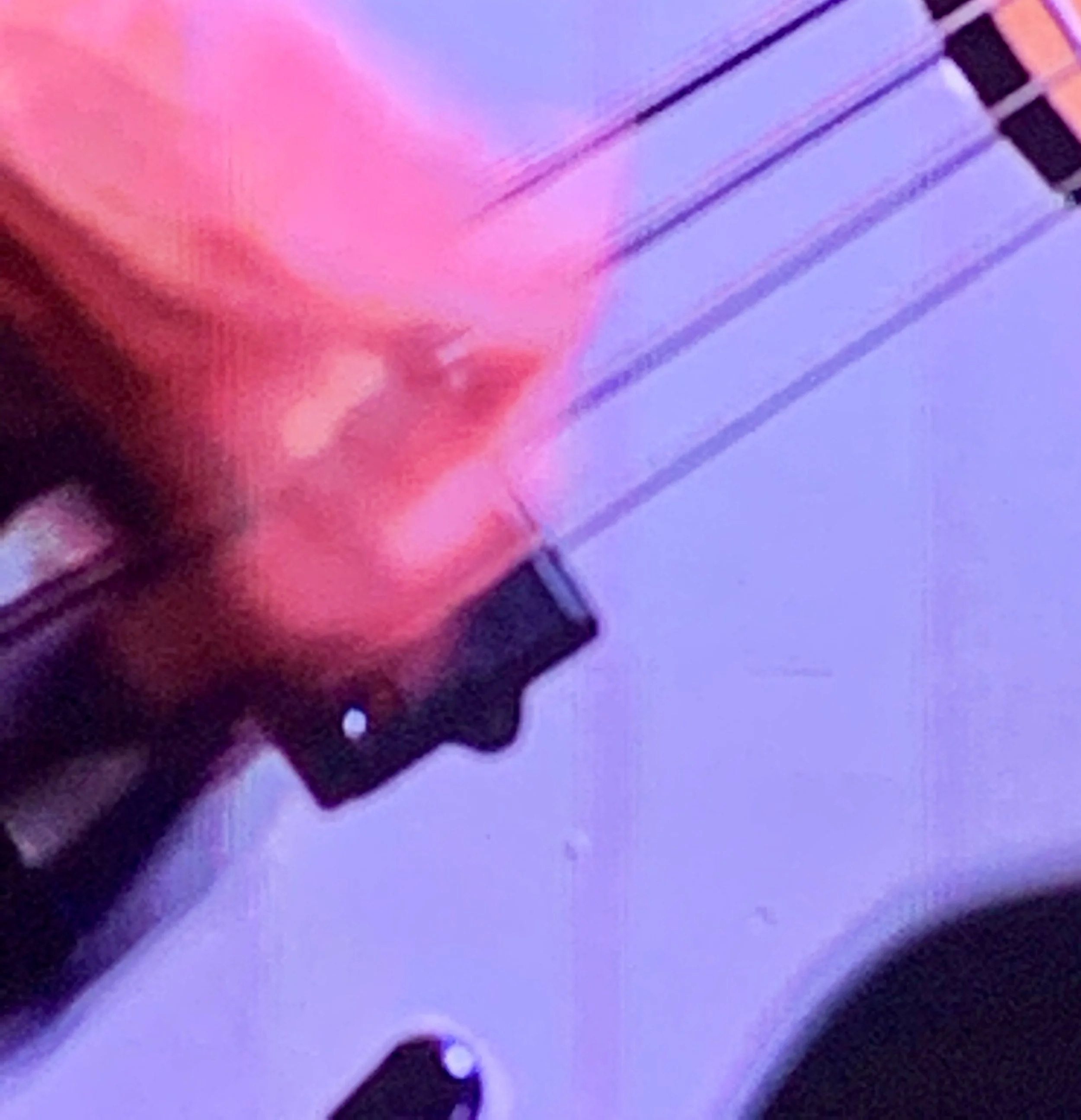 Close-up of a guitar's fretboard with pink and purple lighting reflections.