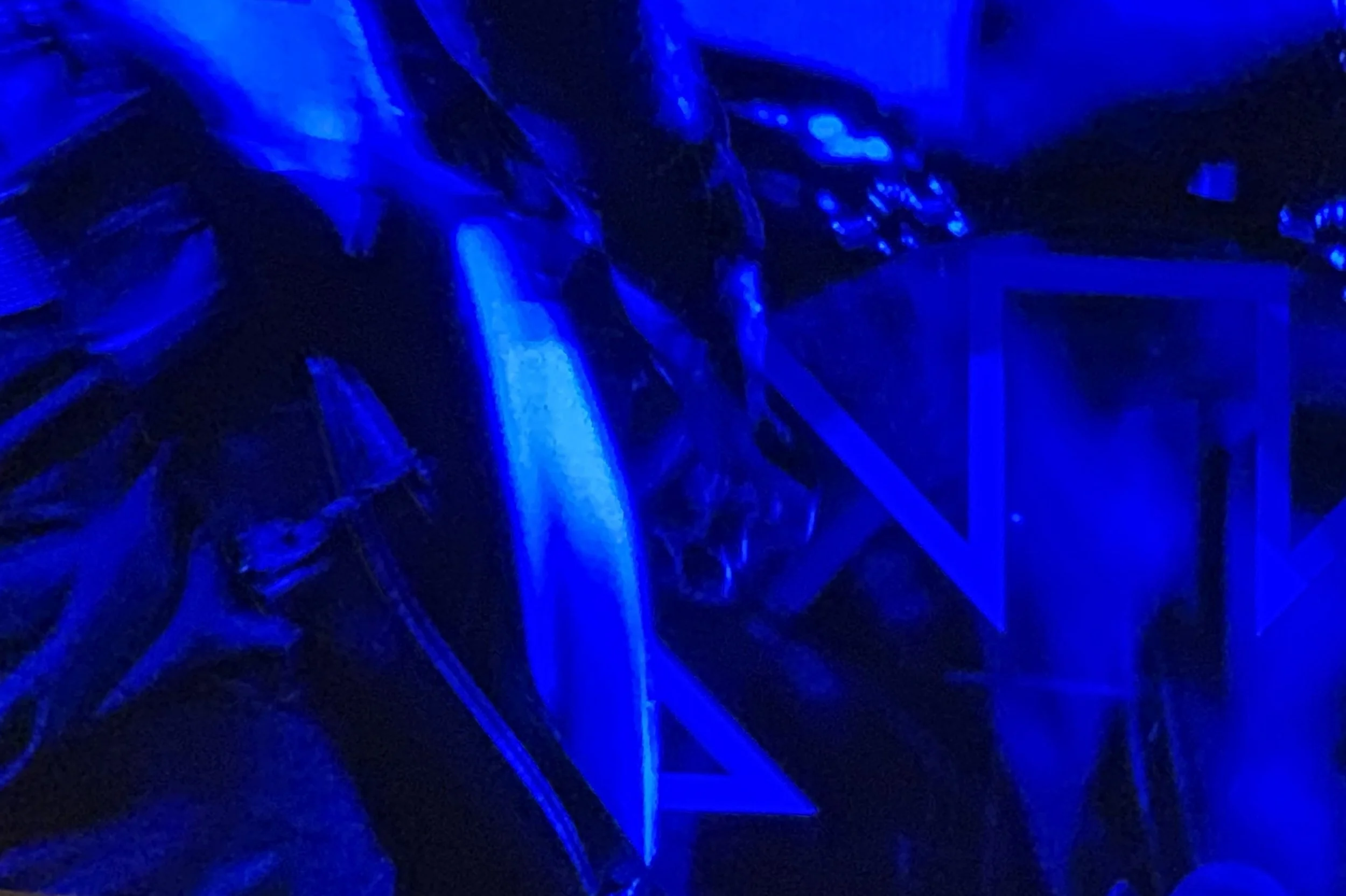 Dark image illuminated by intense blue light, showing abstract shapes and geometric outlines.