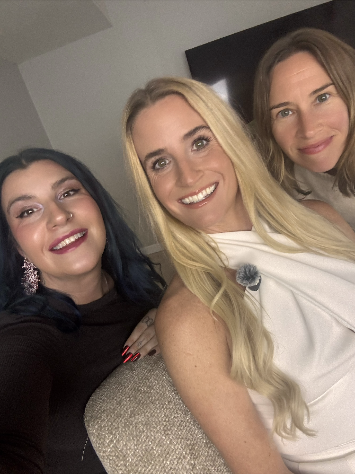 Three women taking a selfie together, smiling, in an indoor setting.
