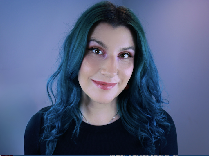 A woman with long, wavy blue hair smiling at the camera.