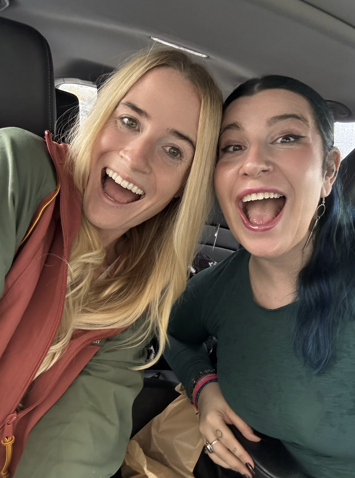 Two women sitting in a car taking a selfie. They are smiling and appear to be happy.