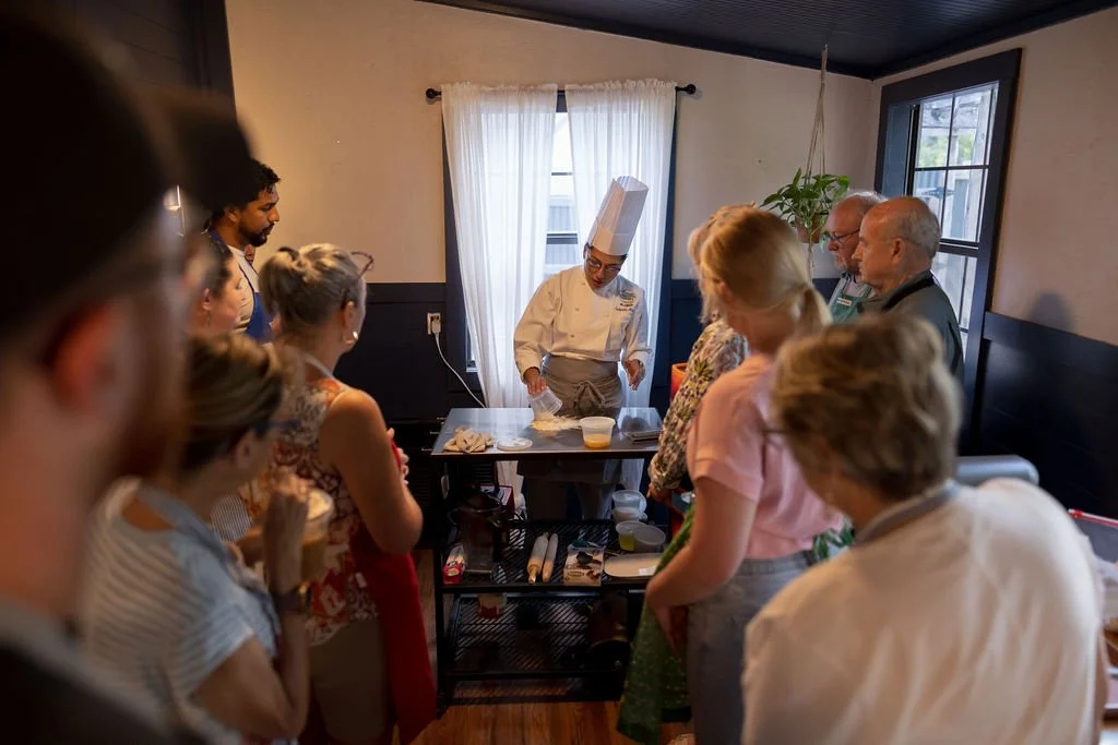 A chef demonstrating cooking techniques to a group of people in a small kitchen or cooking class setting