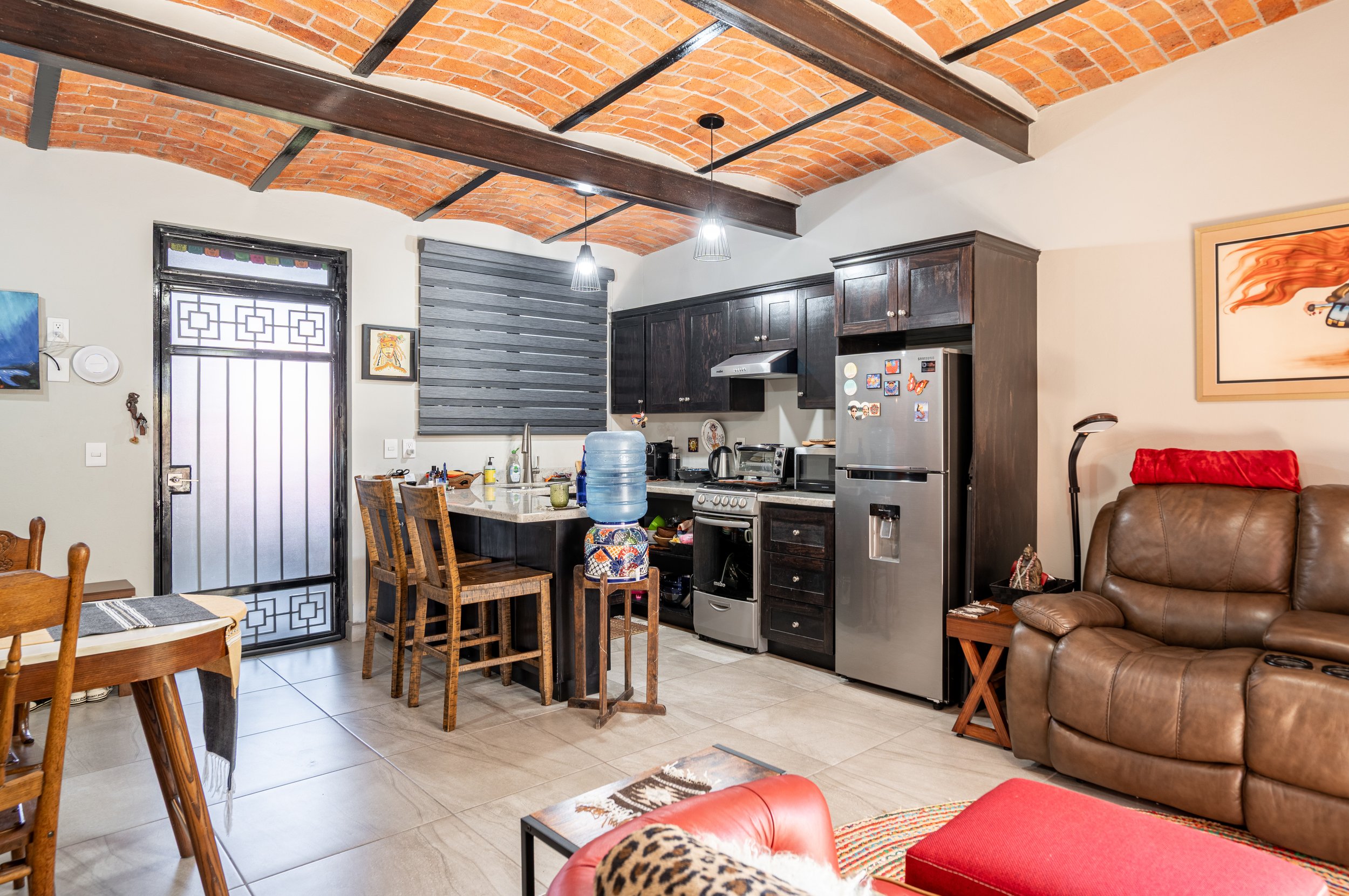 Ajijic rental opportunity. Investment property. Cozy kitchen and living room with brick ceiling, wooden furniture, stainless steel appliances, leather seating, and colorful decor.