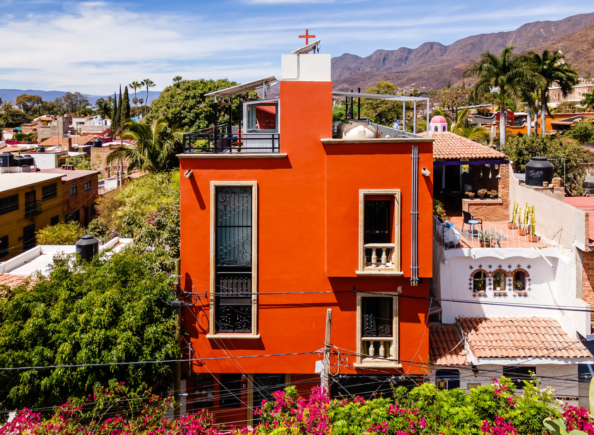 Ajijic rental opportunity. Investment property. Orange building with balcony and cross on roof, surrounded by greenery and mountains in the background.