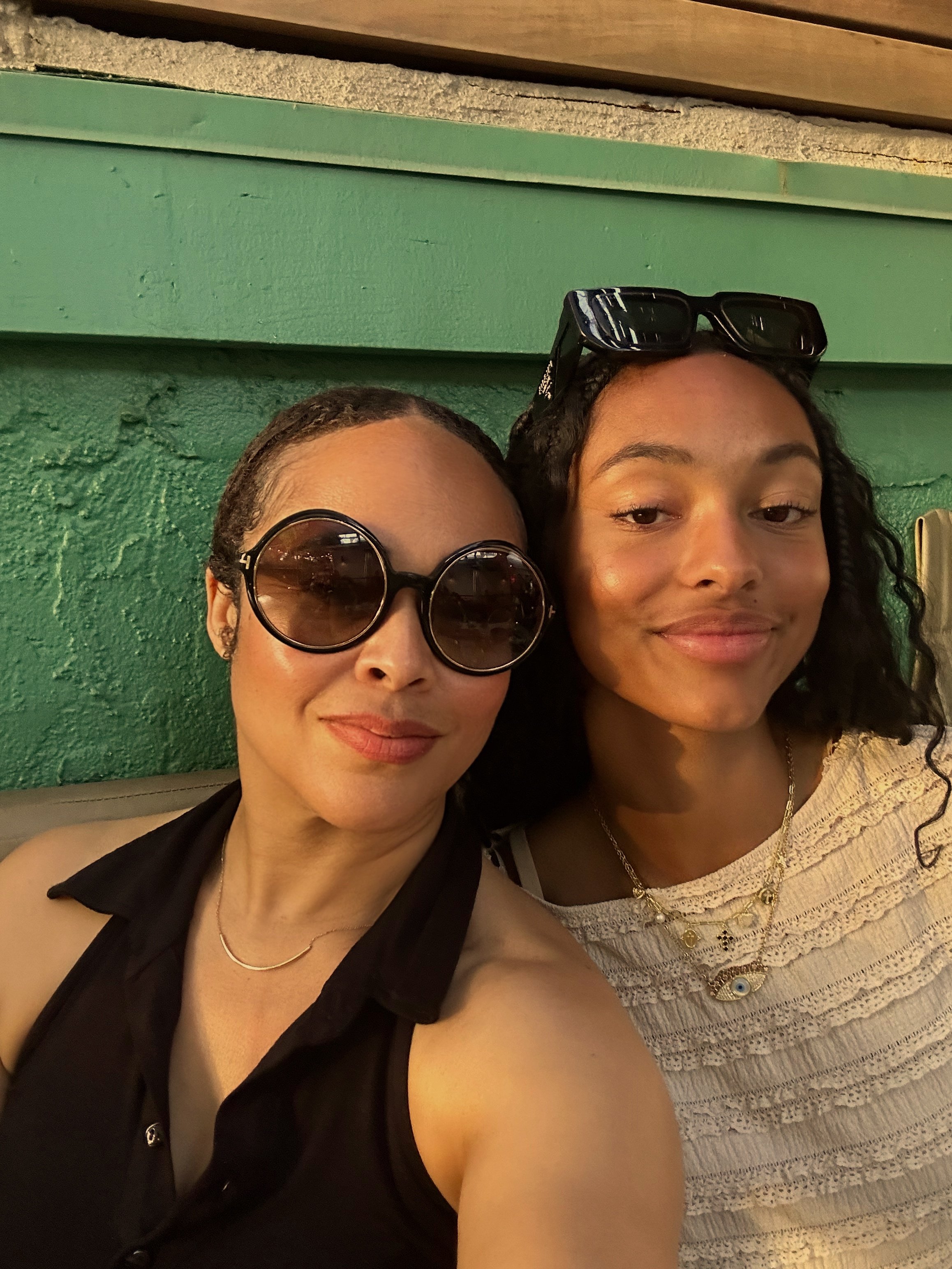 Two women smiling in front of green wall — radiant selfie from Maisha Dyson’s real life lens.