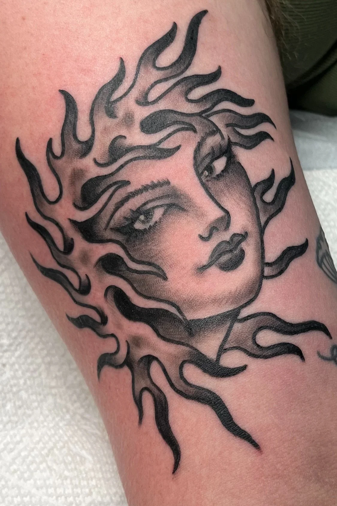 Tattoo of a woman's face with flowing hair, shaded in black and gray, on skin.