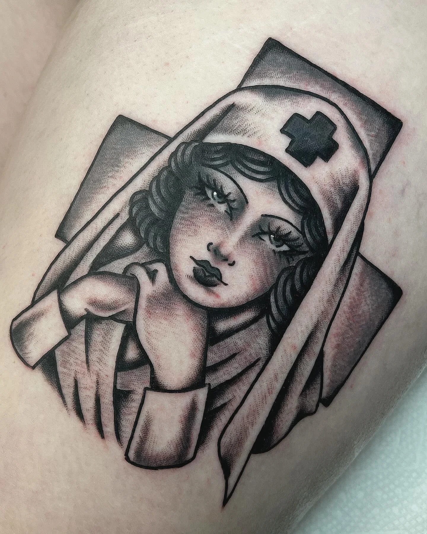 Tattoo of a vintage-style nurse with dark hair, wearing a nurse cap with a cross, resting her head on her hand, in black and gray shading.