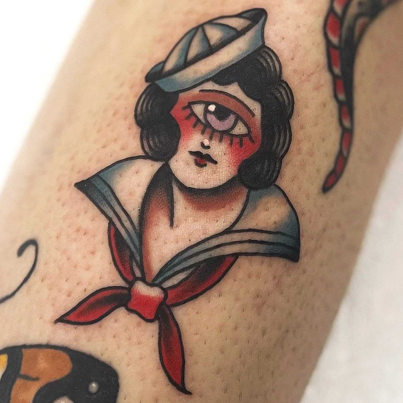 Tattoo of a vintage-style girl with a sailor hat, one eye closed, with makeup and a red neckerchief.