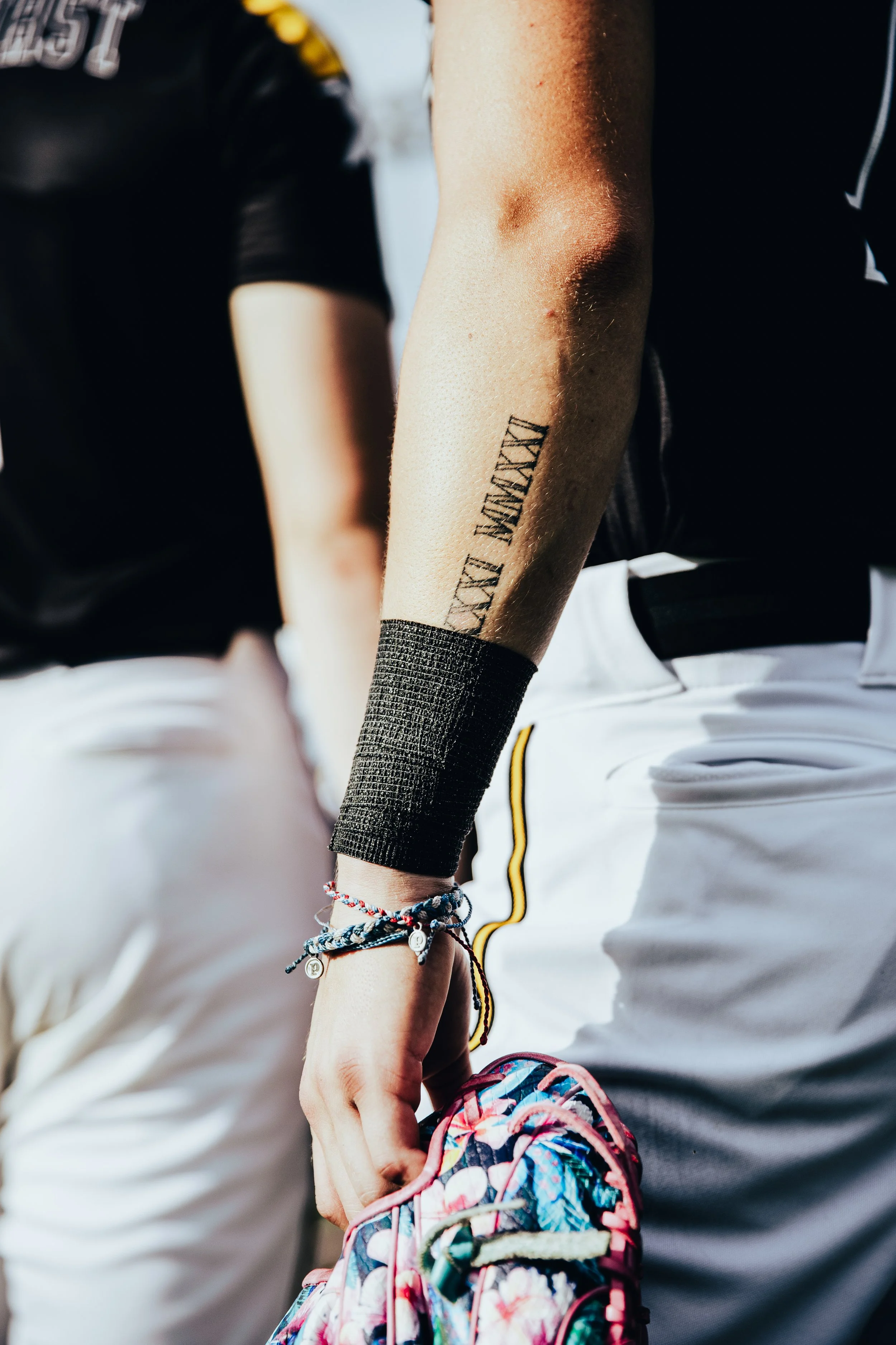 Close-up of a person's arm with a tattoo and several colorful bracelets, holding a floral-patterned backpack.