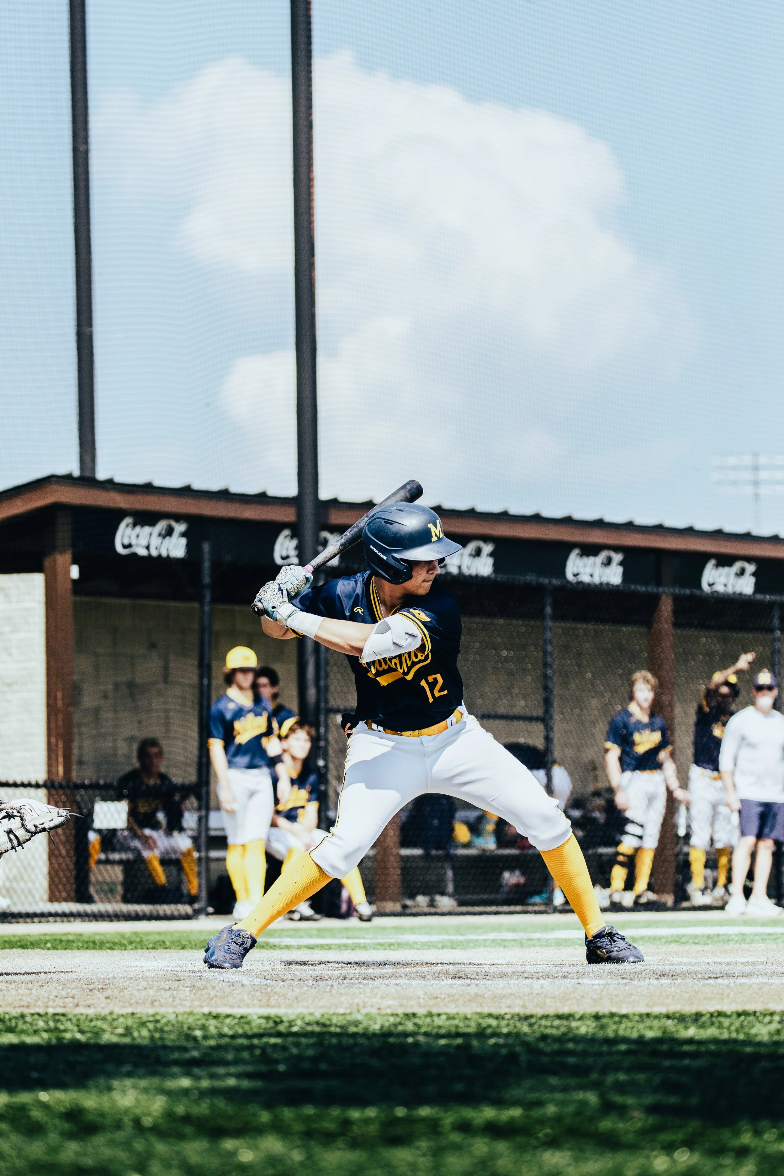 A baseball player in a batting stance at a baseball field with his team and spectators in the background.