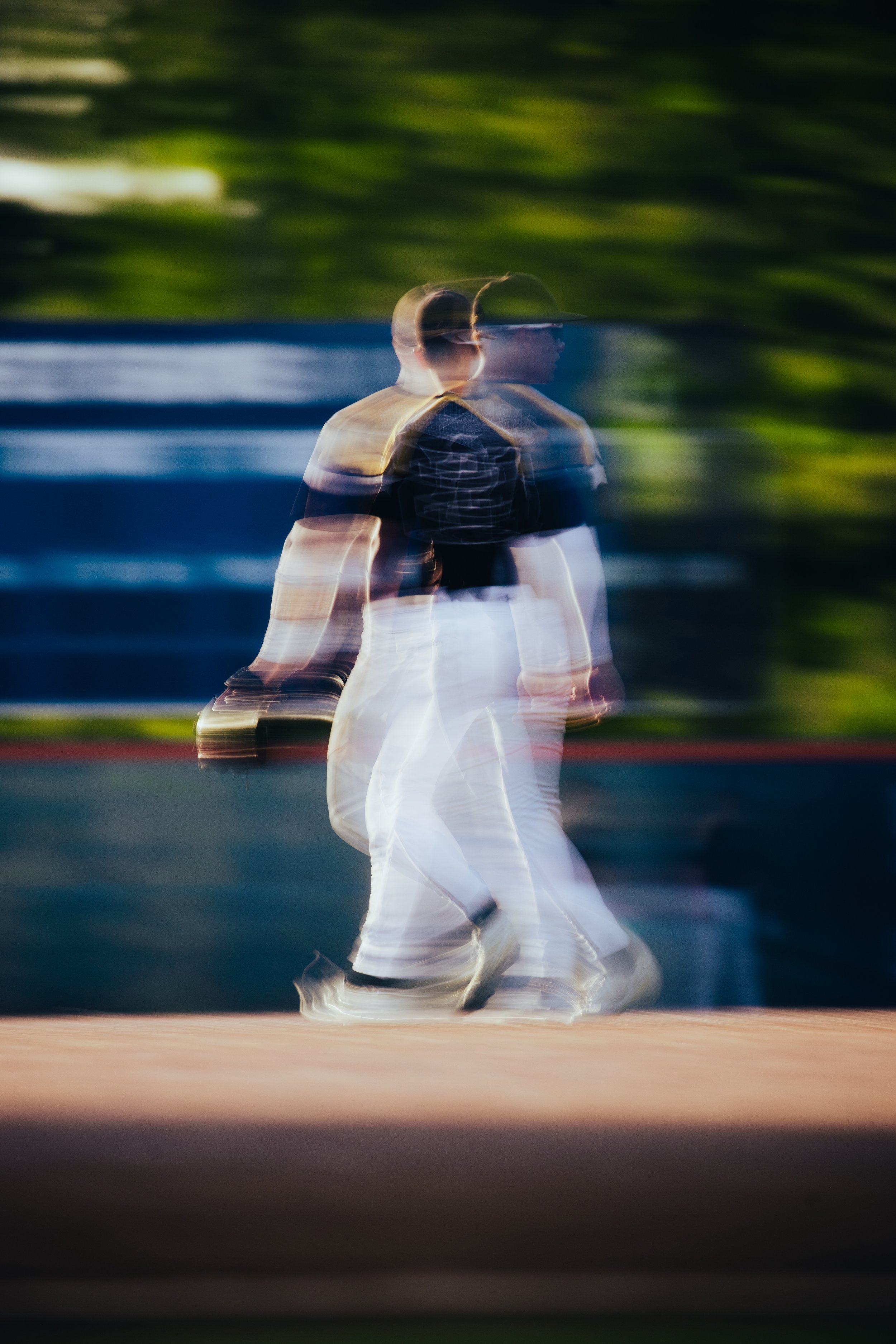 A person walking in front of a blurred background with green trees and blue sky, captured with a motion blur effect.