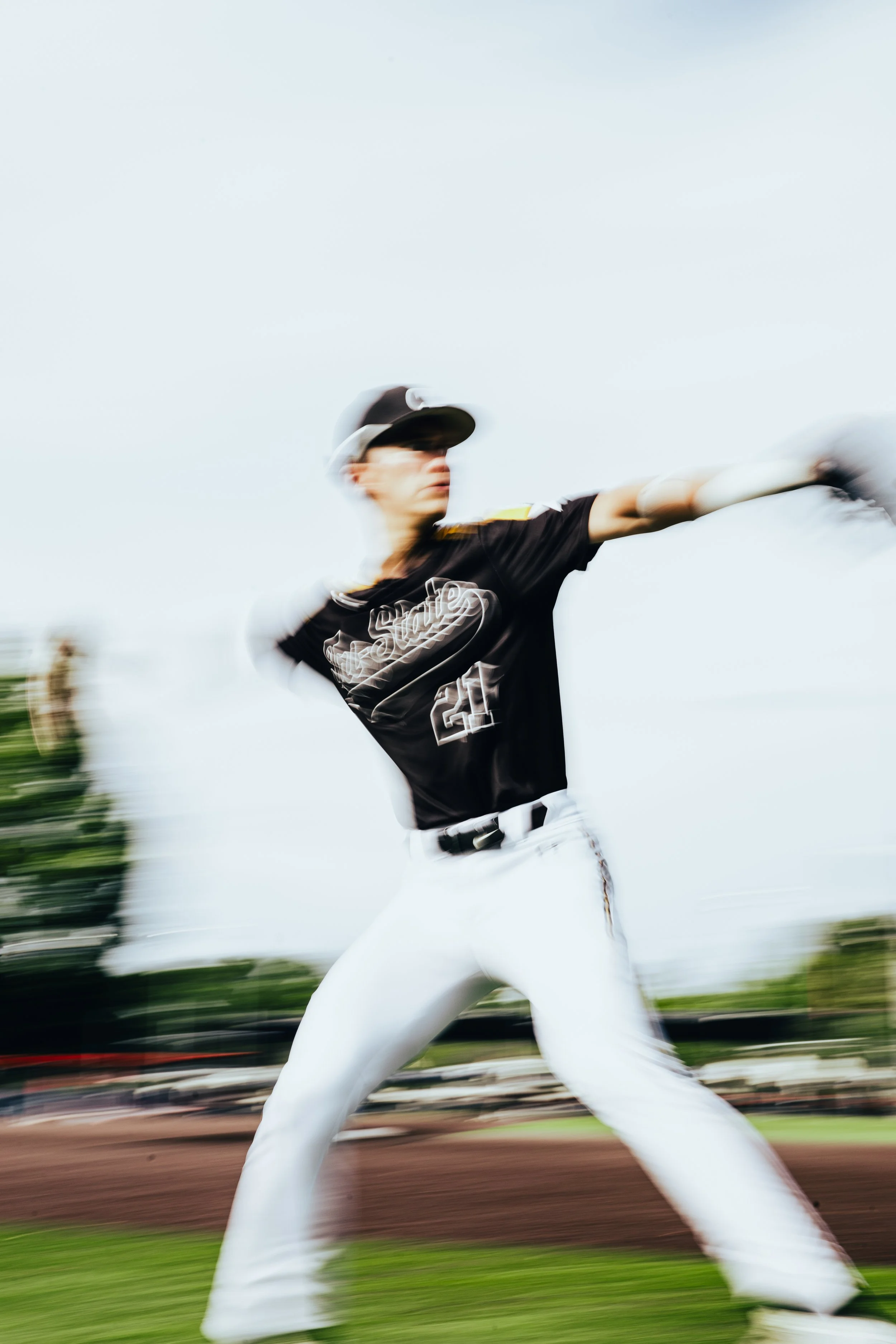 A baseball player swinging a bat on a baseball field, with motion blur and a clear sky in the background.