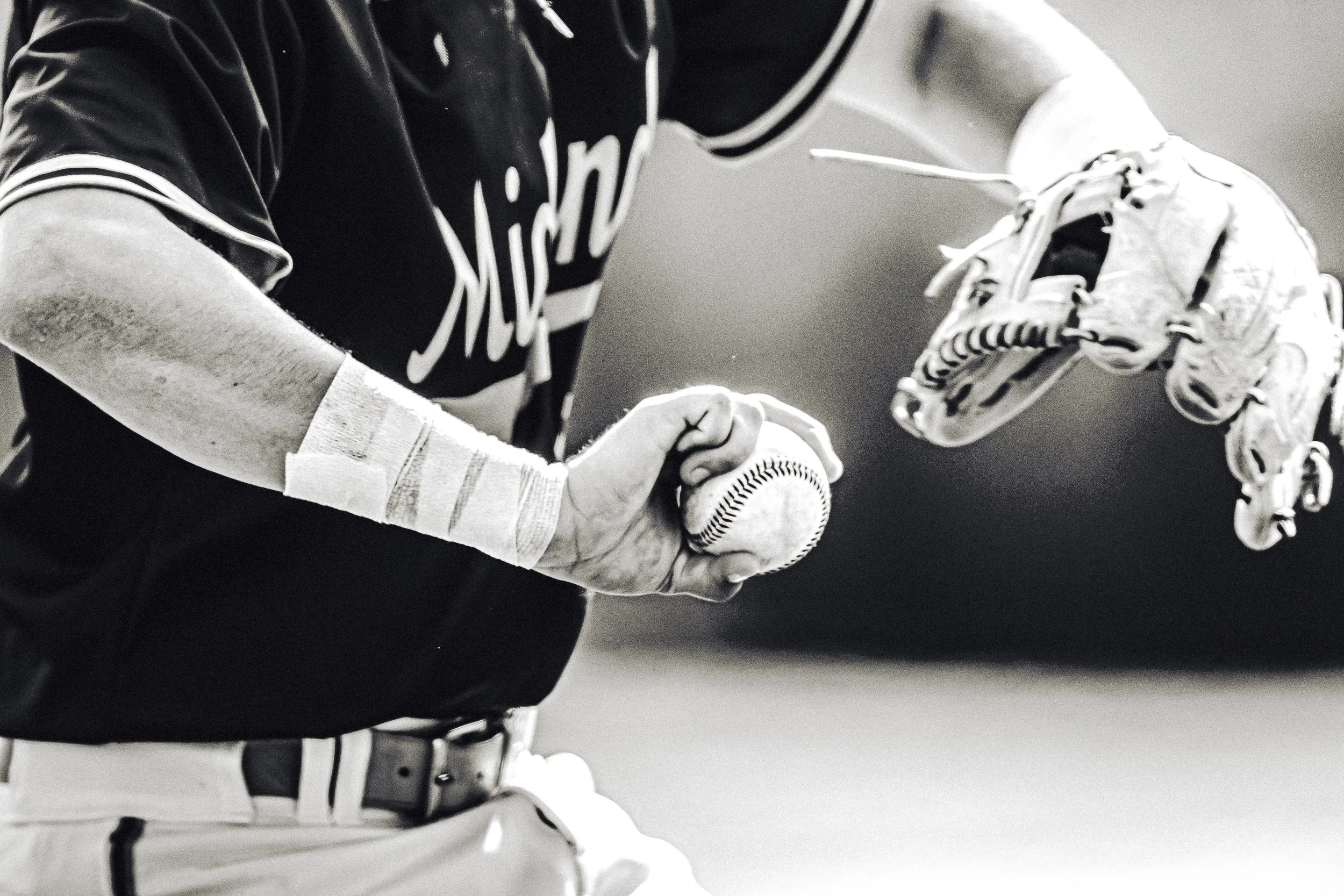 A close-up black and white photograph of a baseball catcher preparing to catch a ball, wearing protective gear and a glove.