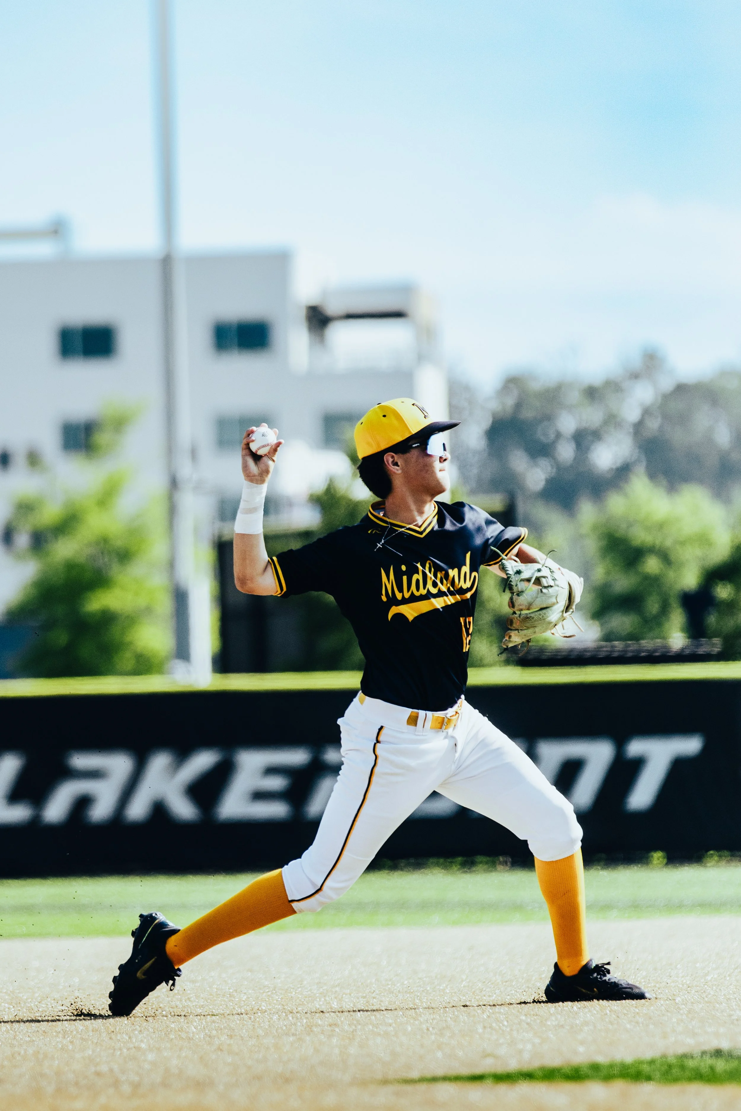 A baseball player in a yellow helmet and black jersey with 'Midland' written on it, throwing a baseball on a field.