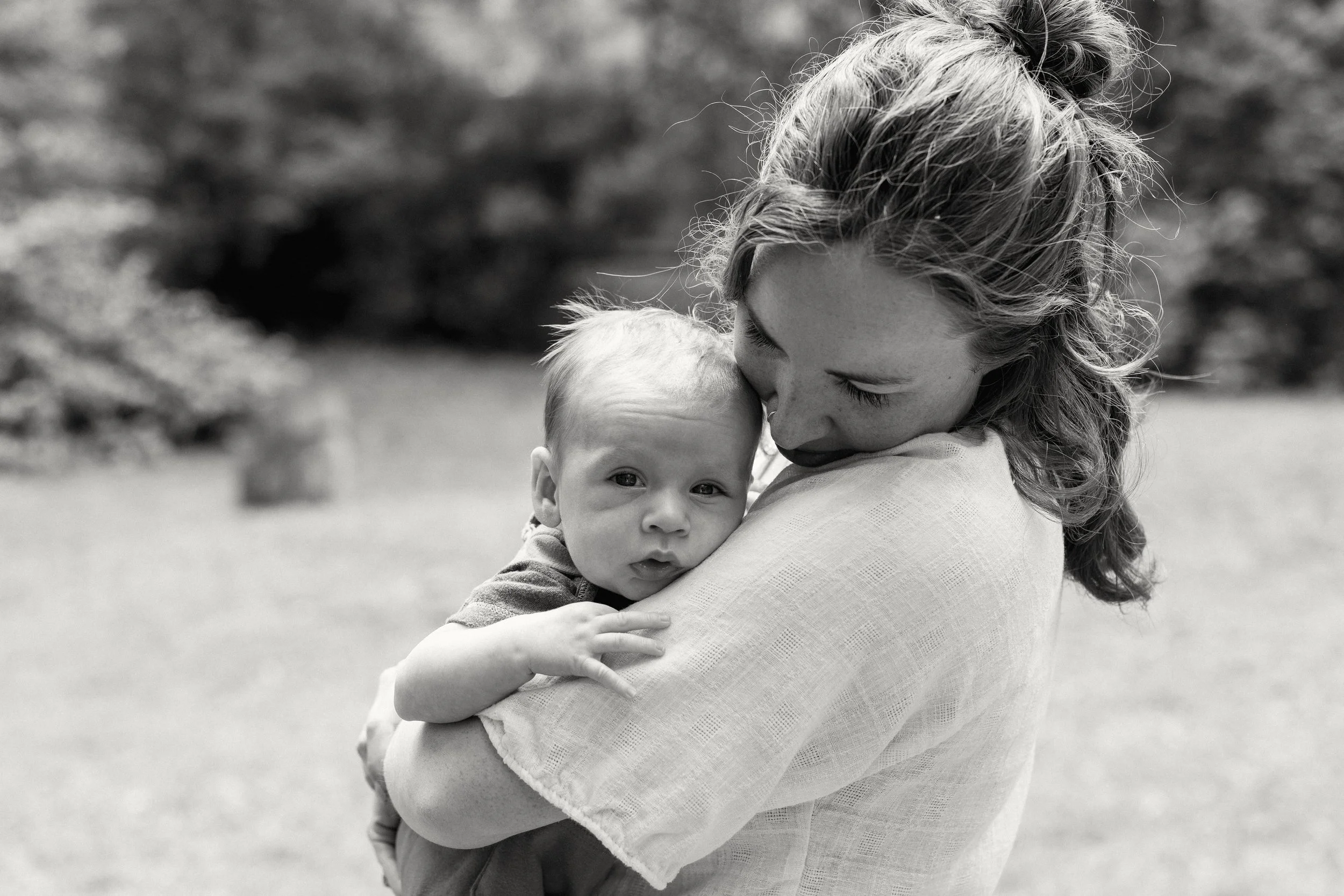 A woman with curly hair holding a young child in her arms outdoors, with a blurred natural background.