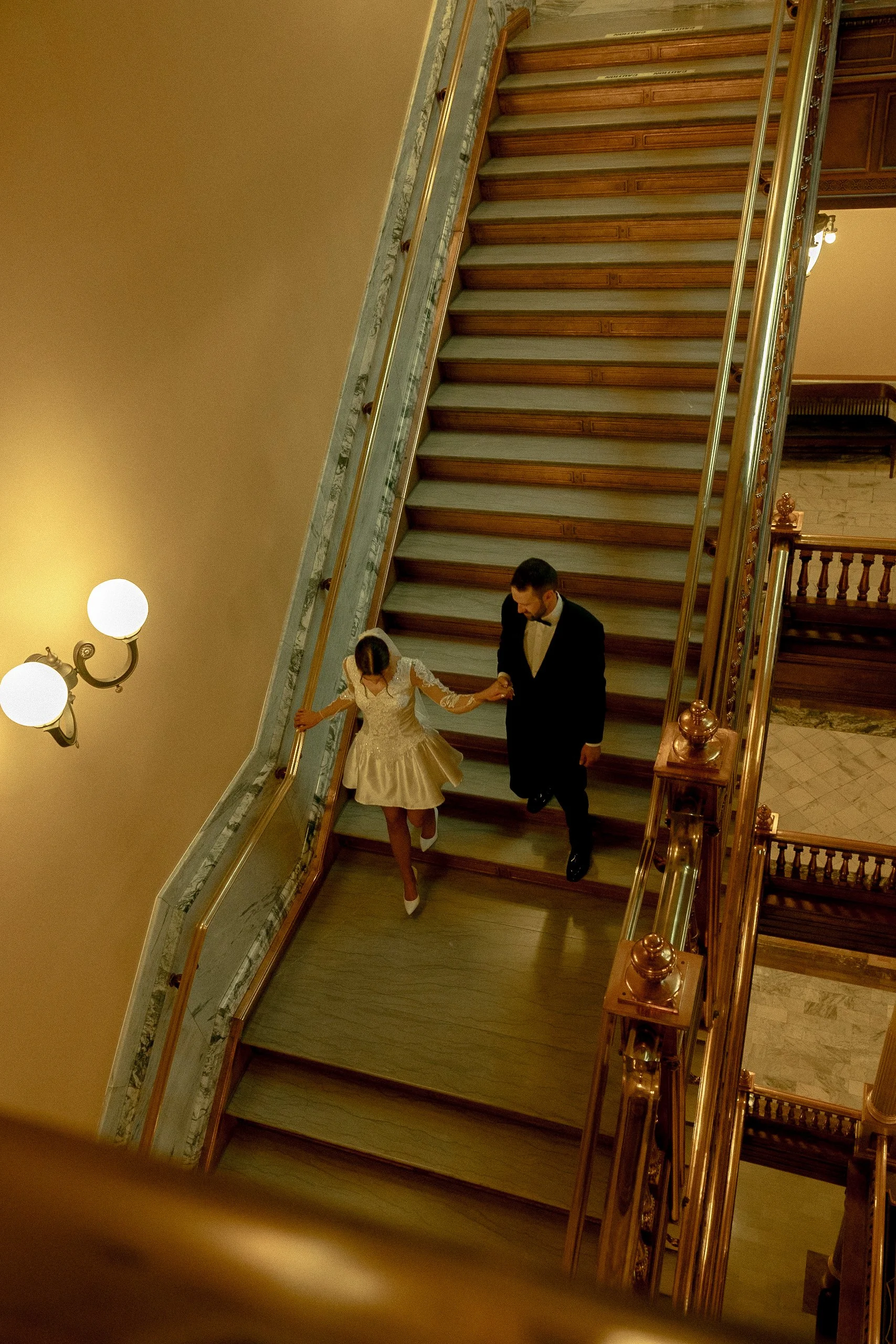Bride and groom walking down the grand staircase inside the Topeka State Capitol.