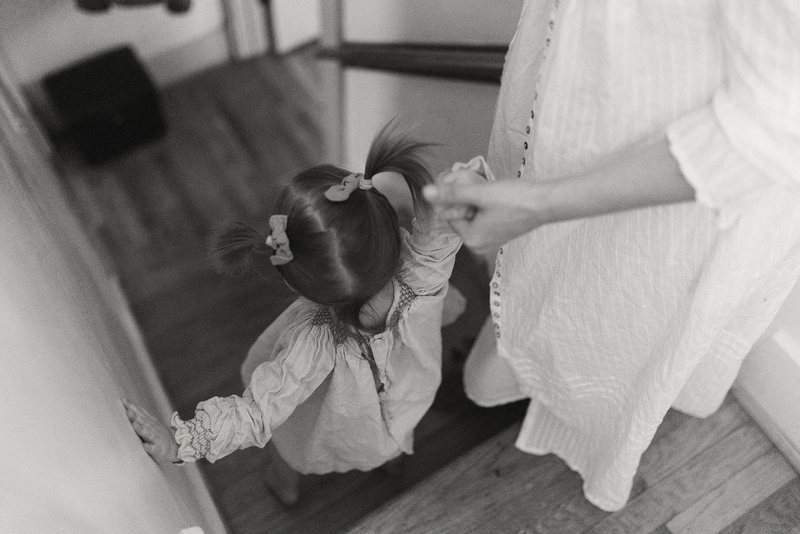 A young girl with pigtails wearing scrunchies, holding the hand of an adult woman, viewed from above on a staircase.