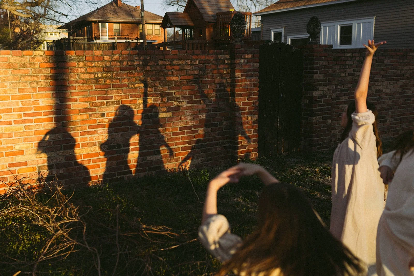 Children playing outside in the evening, casting shadows on a brick wall during sunset.