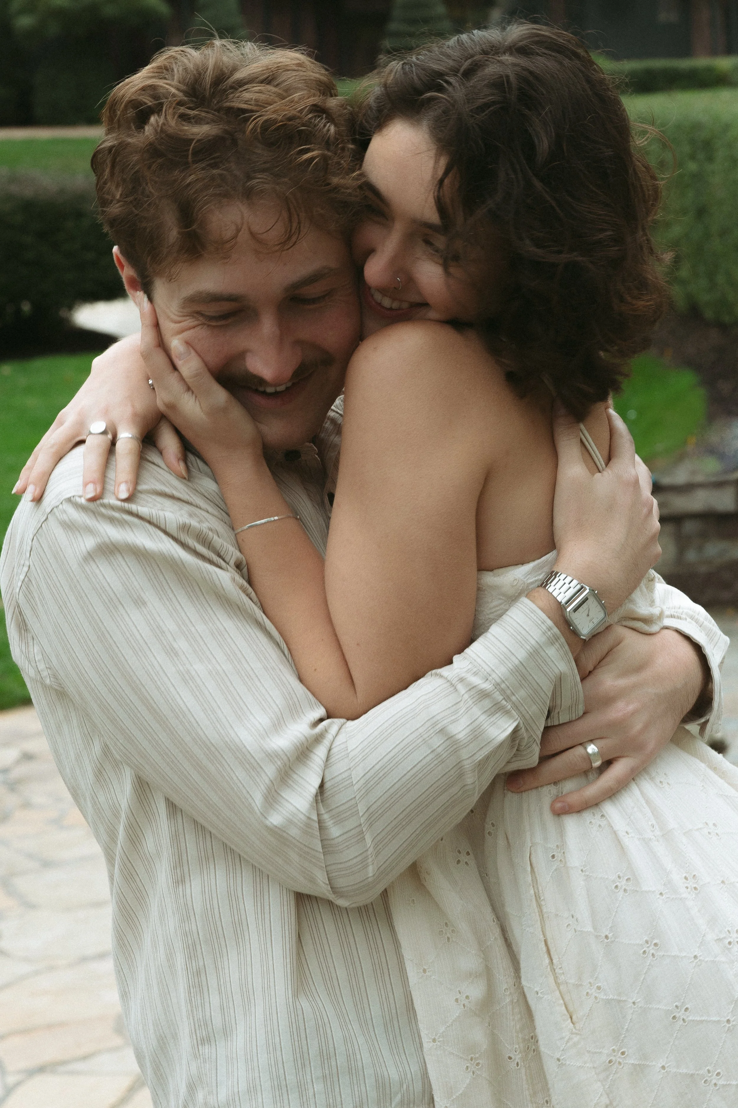 A couple is embracing each other outdoors, smiling and showing affection.
