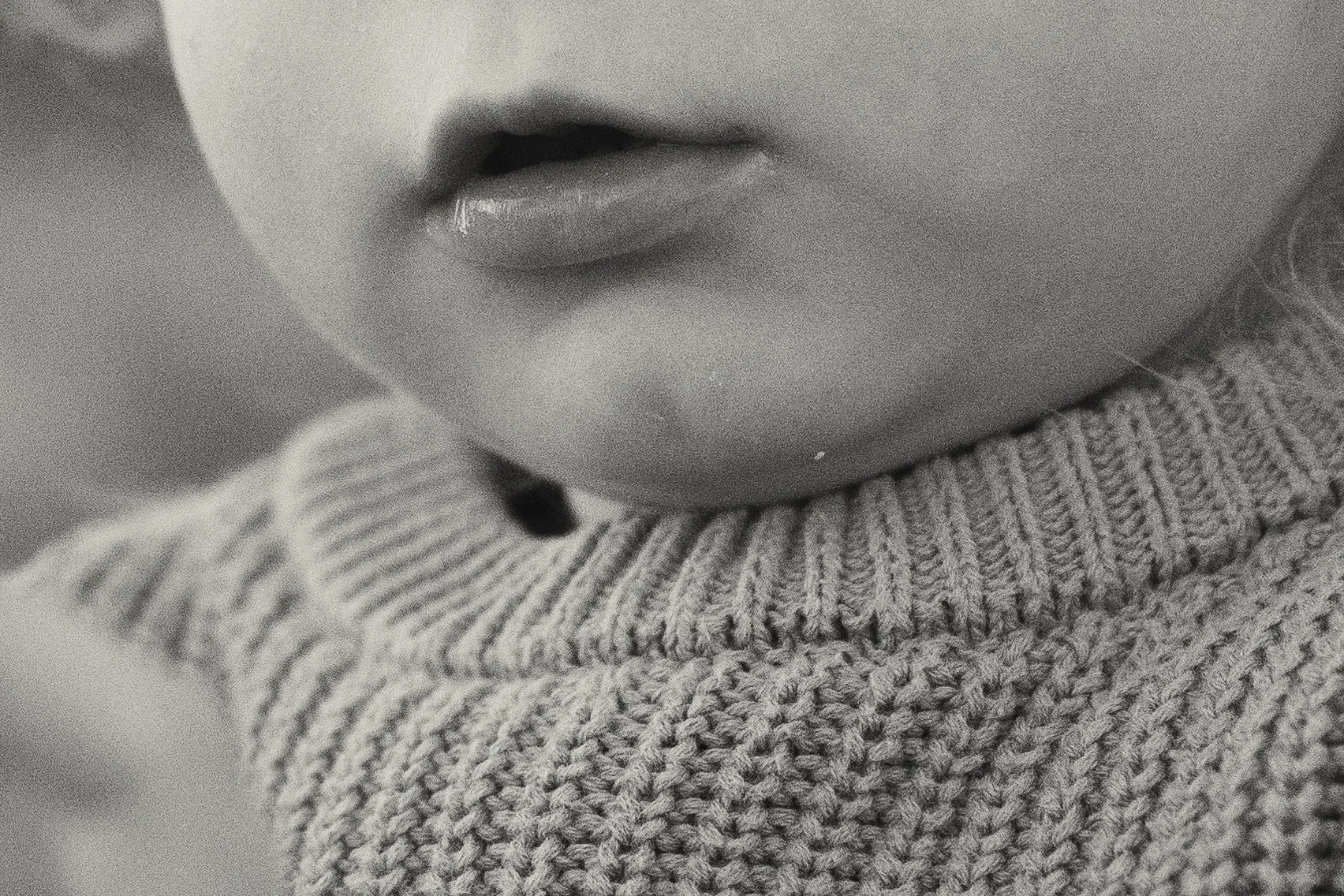 Close-up of a person's lips and chin, wearing a knitted sweater.