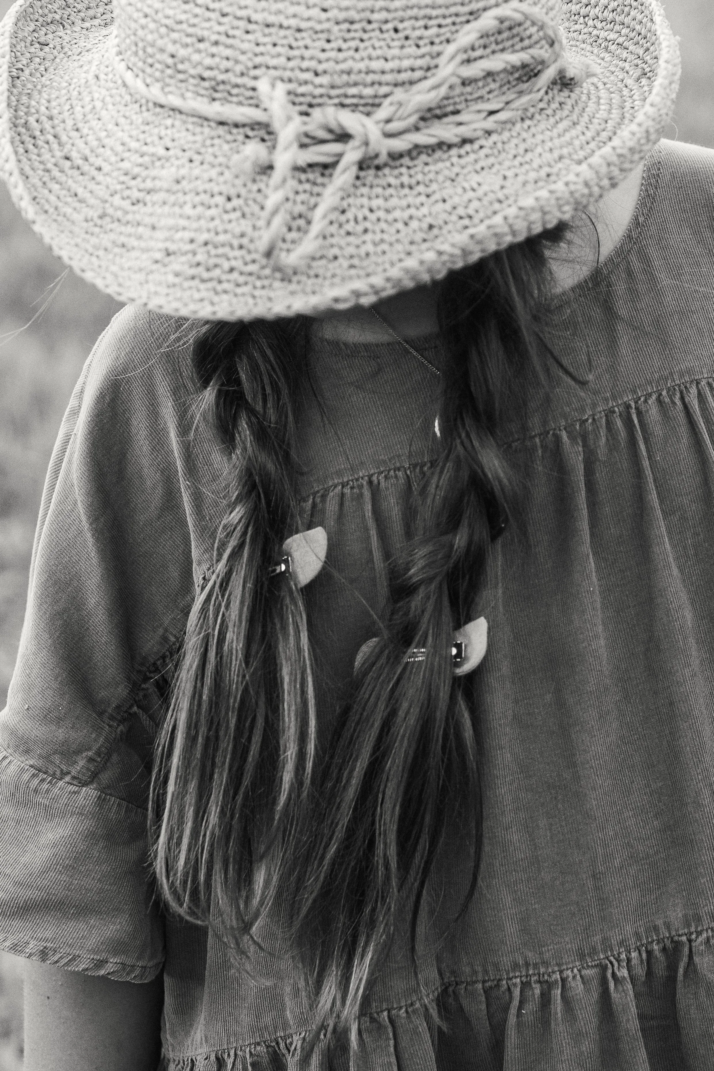 A person with long hair in two braids wearing a wide-brimmed straw hat and a loose, gathered dress.