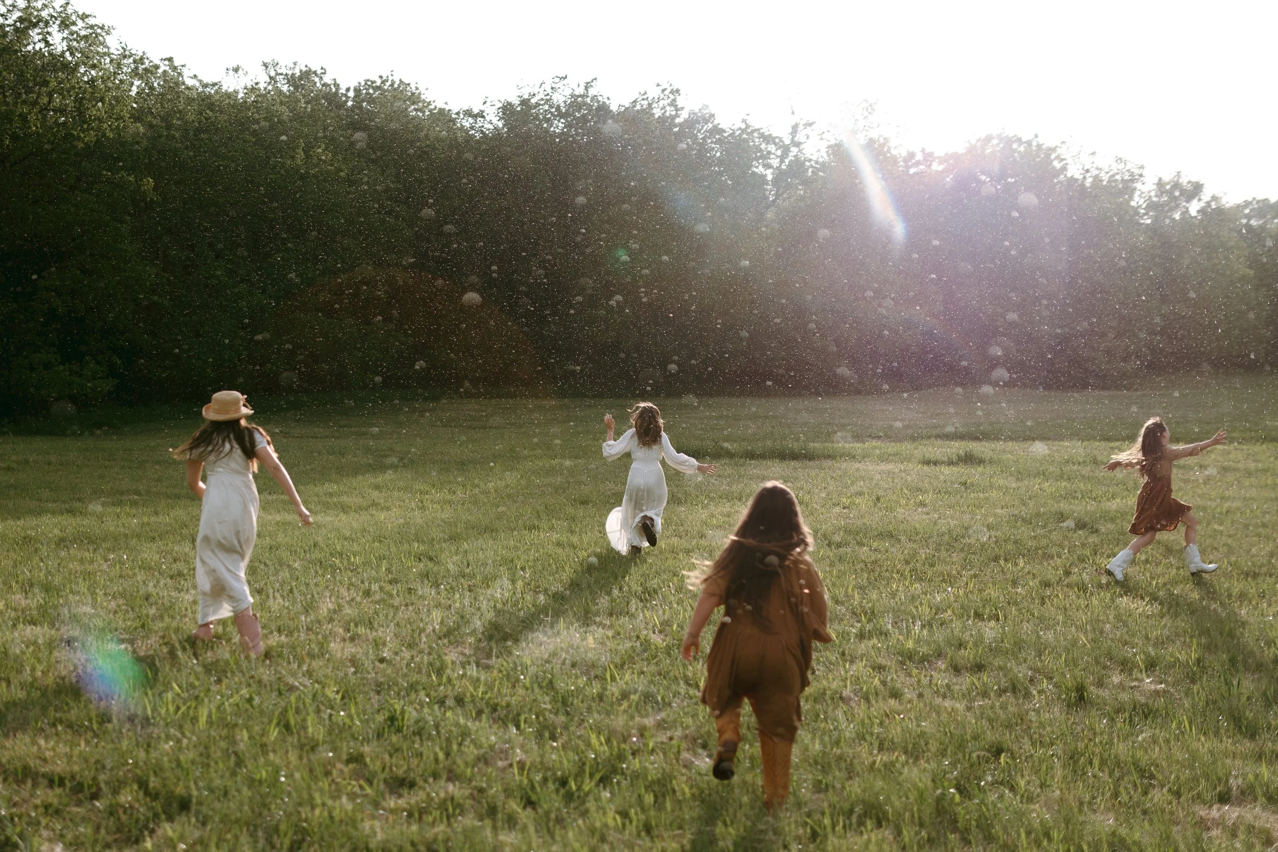 Five children running through a grassy field with trees in the background, sunlight shining from the top right corner.