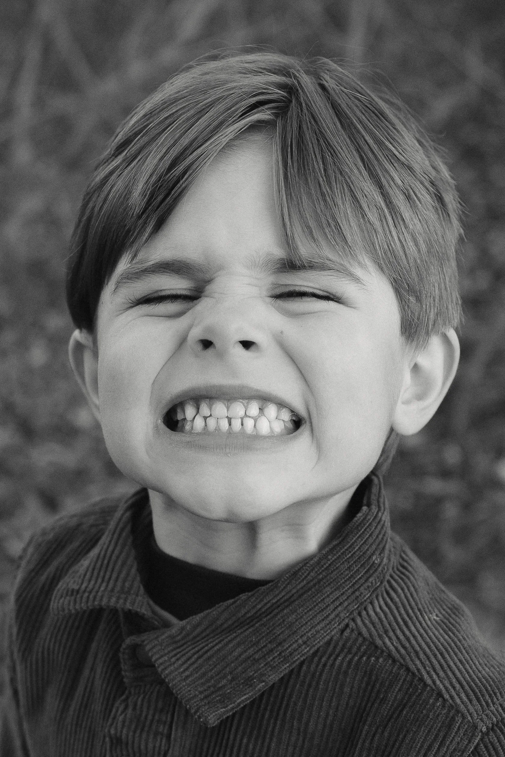 A young boy with a big grin, showing his teeth, outdoors.