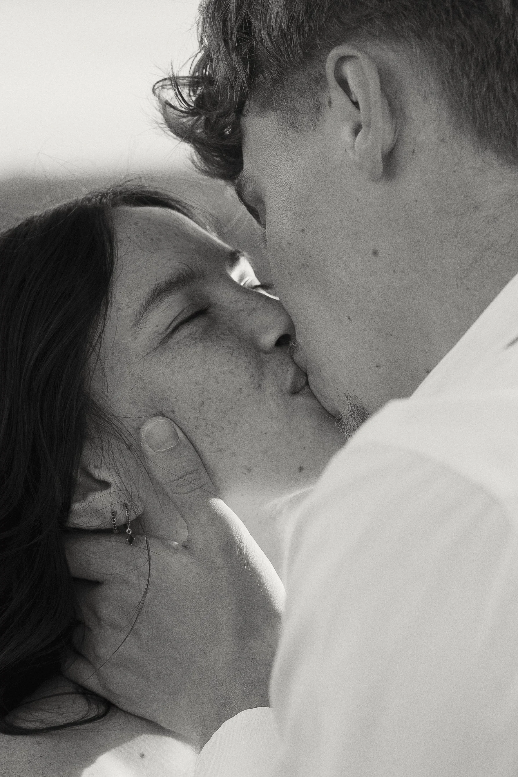 A black-and-white photograph of a couple sharing a close, intimate moment, with their foreheads and noses touching and their eyes closed.