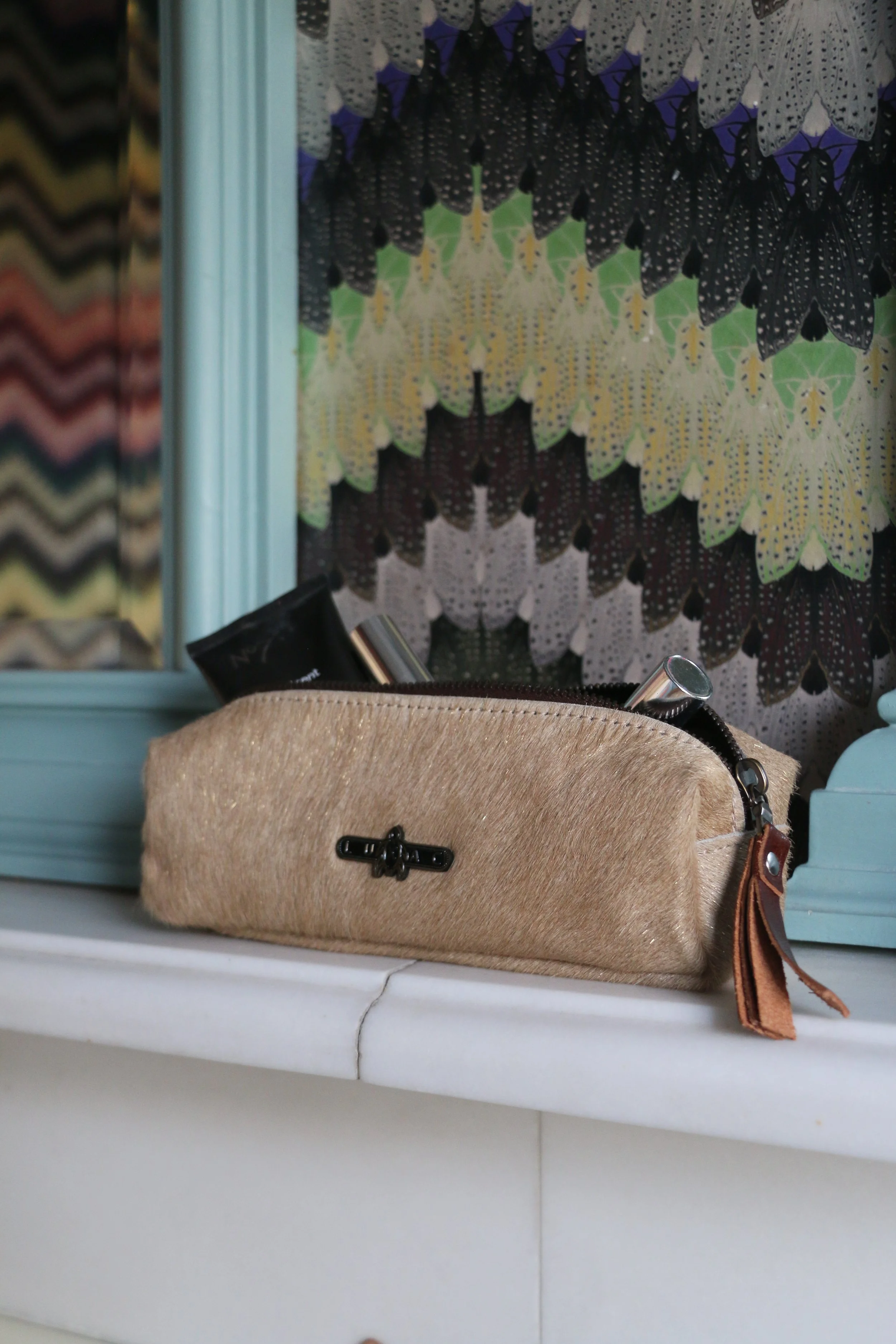 A beige fabric makeup bag with a zipper, sitting on a white surface, with a butterfly-patterned background and a mirror.