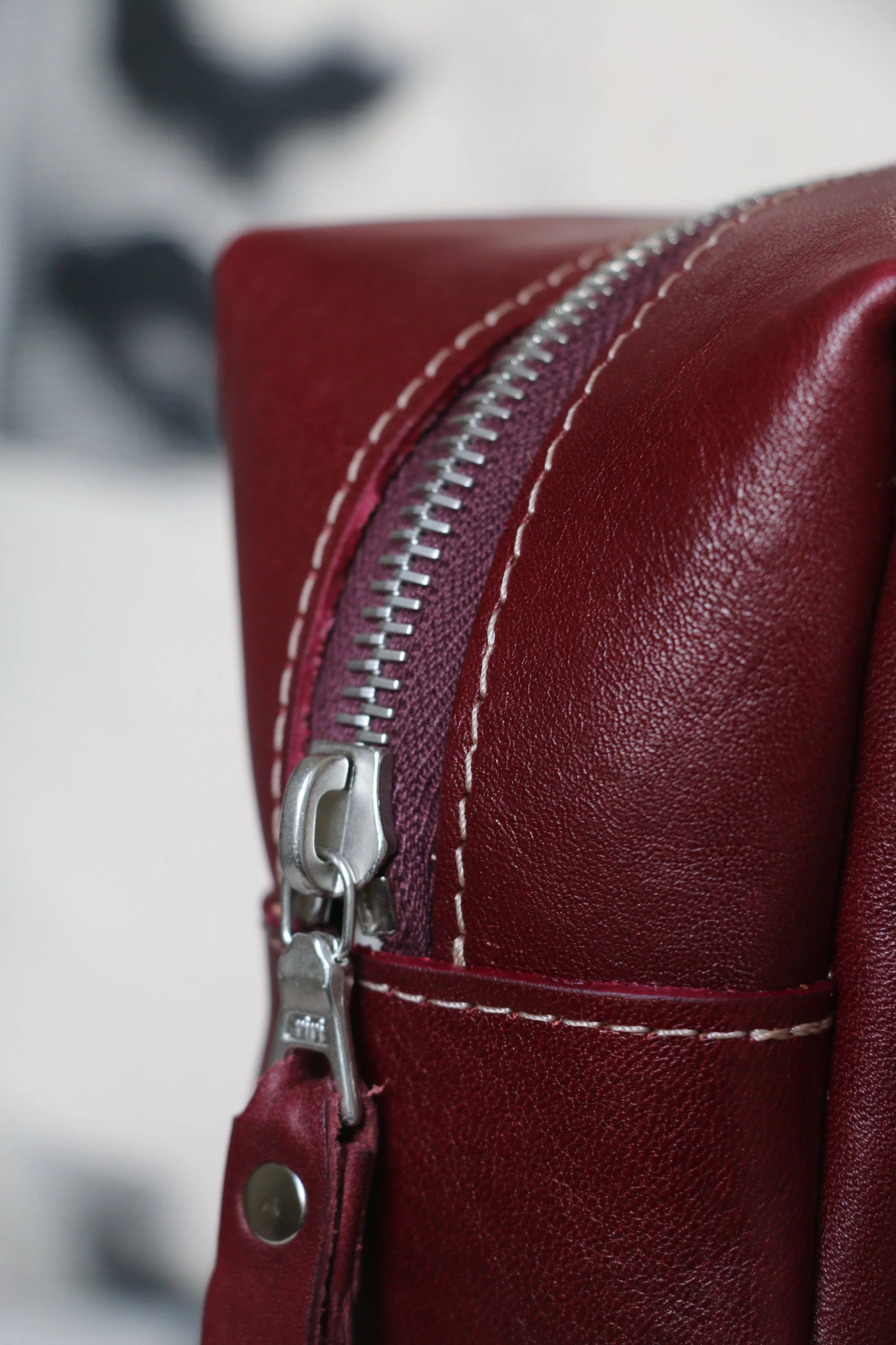 Close-up of a red leather bag with a silver zipper and white stitching.