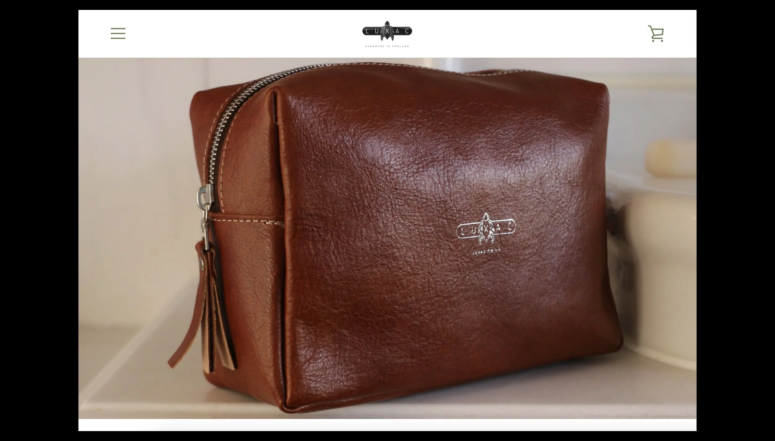 A brown leather toiletry bag with a silver zipper and a small logo featuring a bee, the brand name Luzac on a white surface.