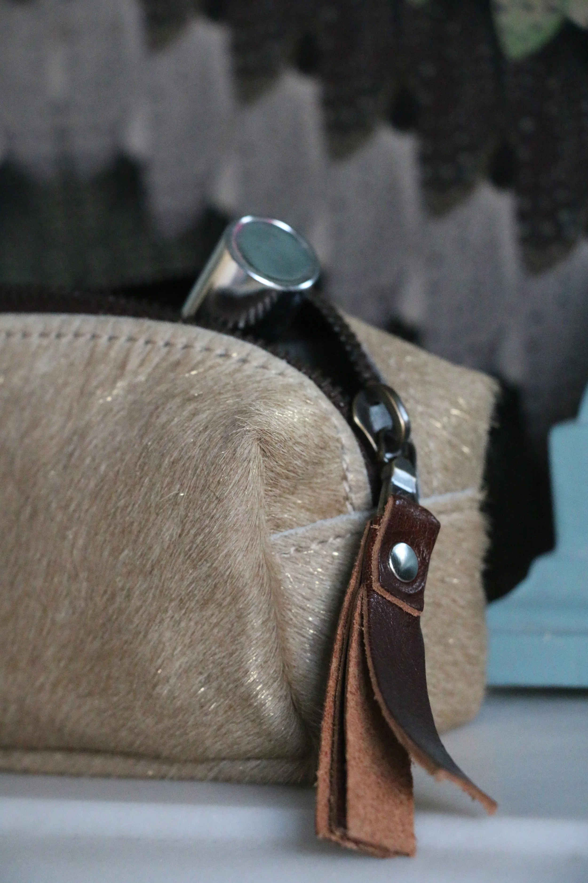 Close-up of a beige bag with a brown leather strap, silver snap, and zipper, with a shiny metal object partially visible inside the bag.