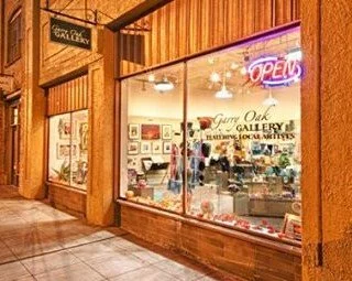 Street scene with a storefront called Gene Oak Gallery, illuminated signs, parked cars, and trees with fall foliage.