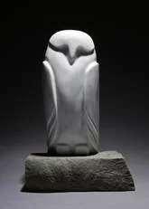 A white carved stone sculpture on a gray base, resembling an abstract or stylized figure or animal.