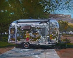 A shiny, vintage silver camper trailer parked on a dirt road with trees and a landscape in the background.