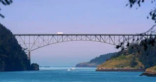 A large bridge spanning over a wide river or waterway, with green hills on either side under a clear sky.