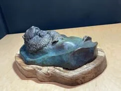 A rock sculpture carved to resemble a reclining human head, resting on a wooden base.