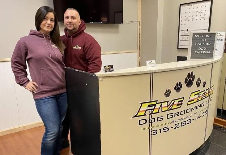 A woman and a man standing behind a reception desk at Five Star Dog Grooming, with a sign and paw print decorations in the background.