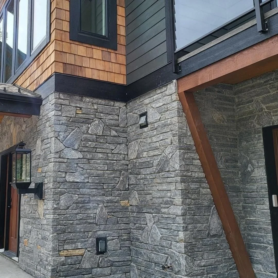 Close-up of a building's exterior featuring a stone wall, wood siding, and black metal accents.