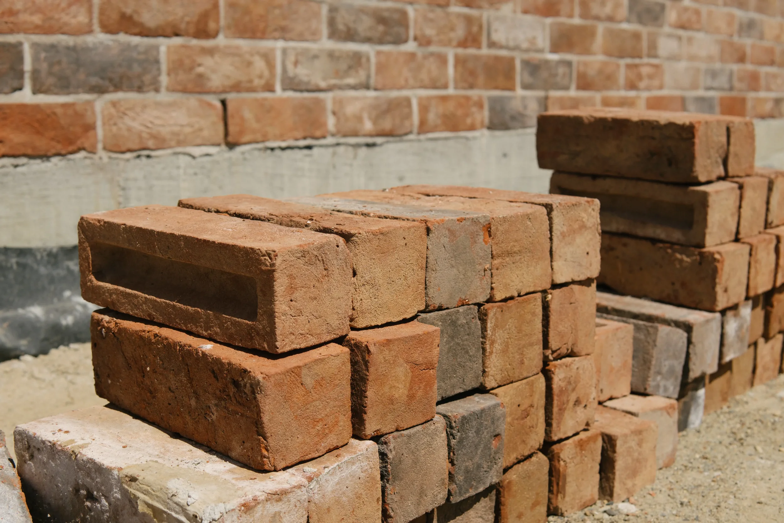 Stacked red bricks in front of a partially finished brick wall.